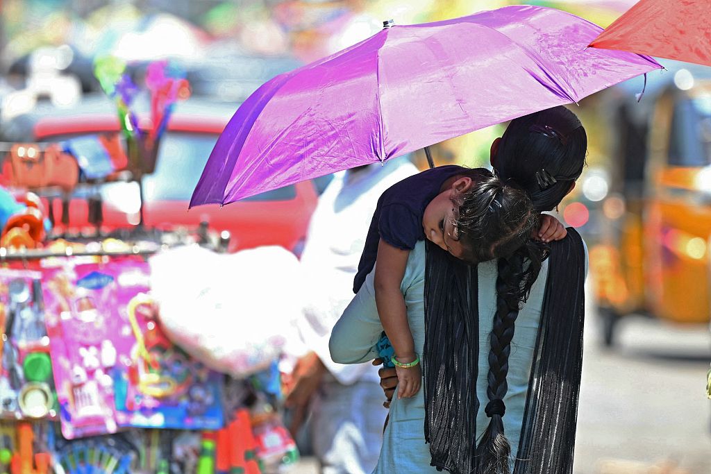 A woman along with her daughter carries an umbrella while walking through a market on a hot summer day in Hyderabad, India, April 25, 2024. /CFP