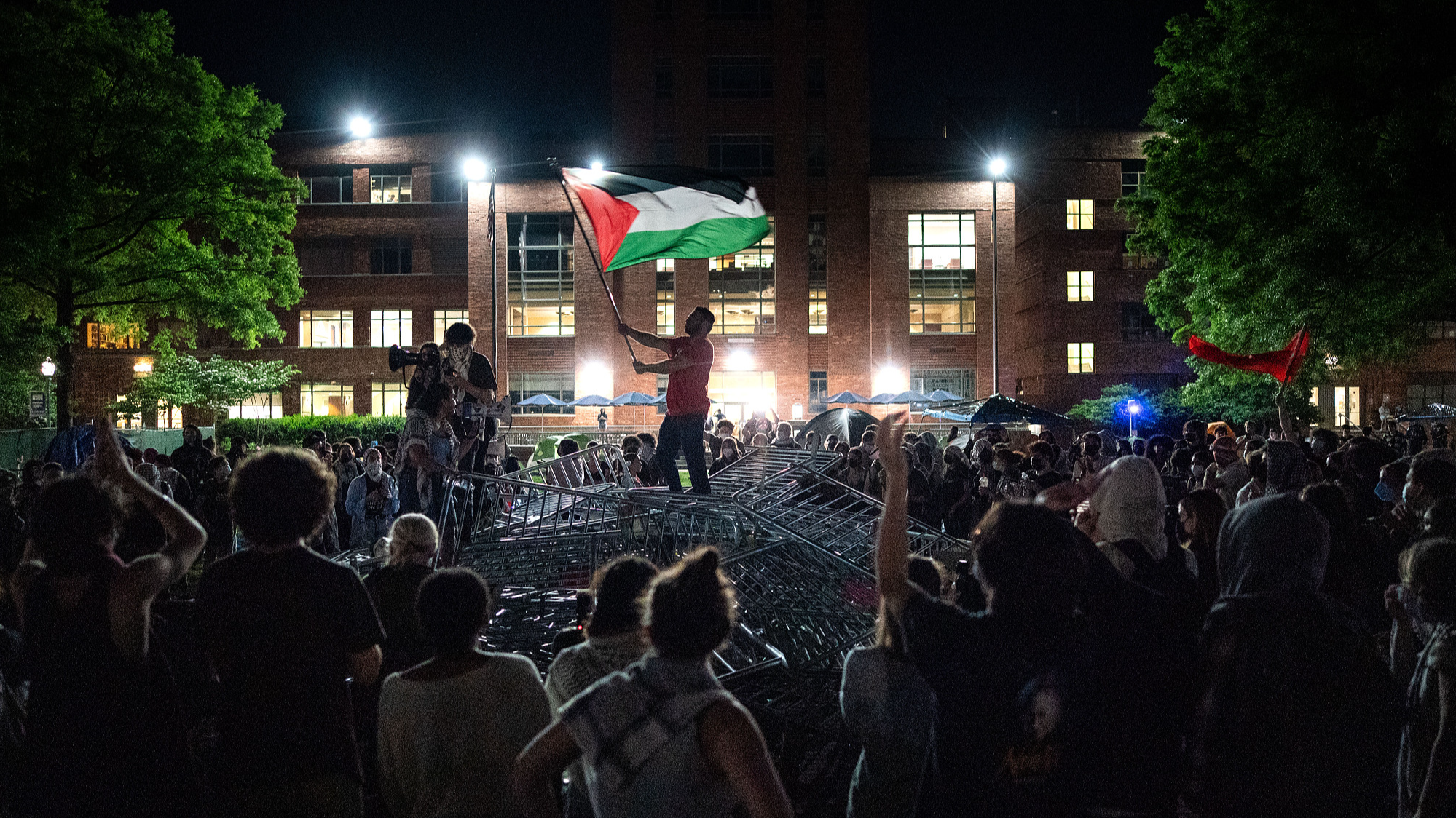 A man holds up a Palestinian flag as activists and students chant, surrounding piled barricades at an encampment at George Washington University in Washington, D.C., U.S., April 29, 2024. /CFP