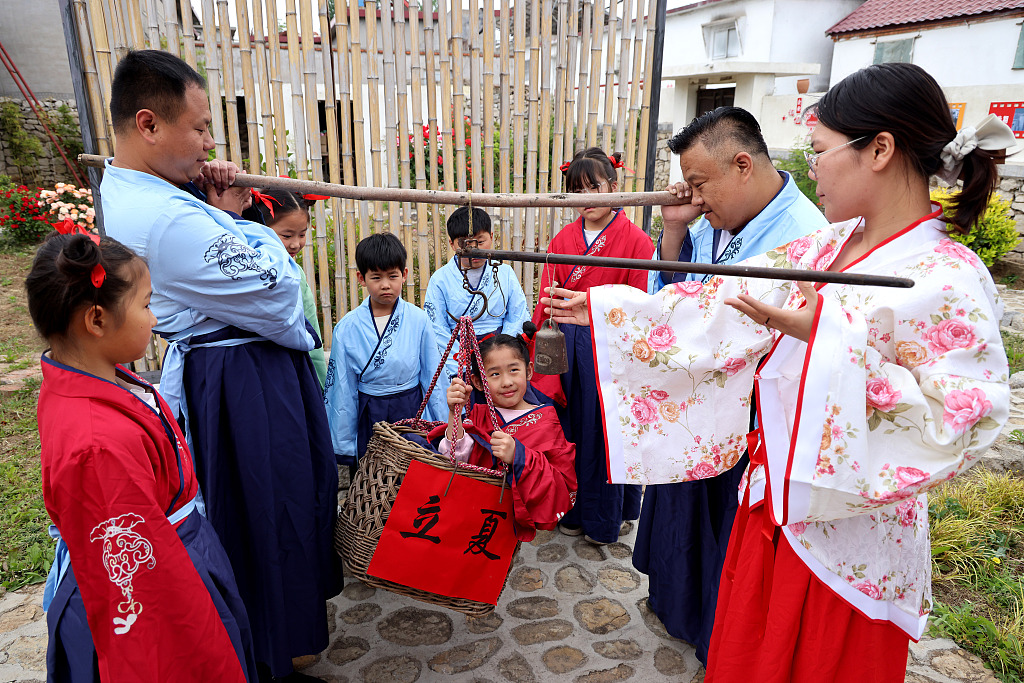 Residents in traditional garments weigh their children on May 4, 2024 ahead of the Start of Summer solar term. As people are more likely to lose weight in summer, this practice is believed to bring health to those being weighed. /CFP