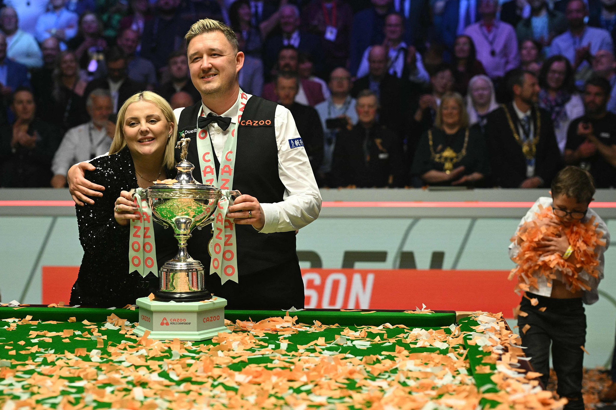 Kyren Wilson poses with the trophy and his wife Sofie as his son Finley (R) collects the confetti after winning the World Snooker Championship final in Sheffield, England, May 6, 2024. /CFP