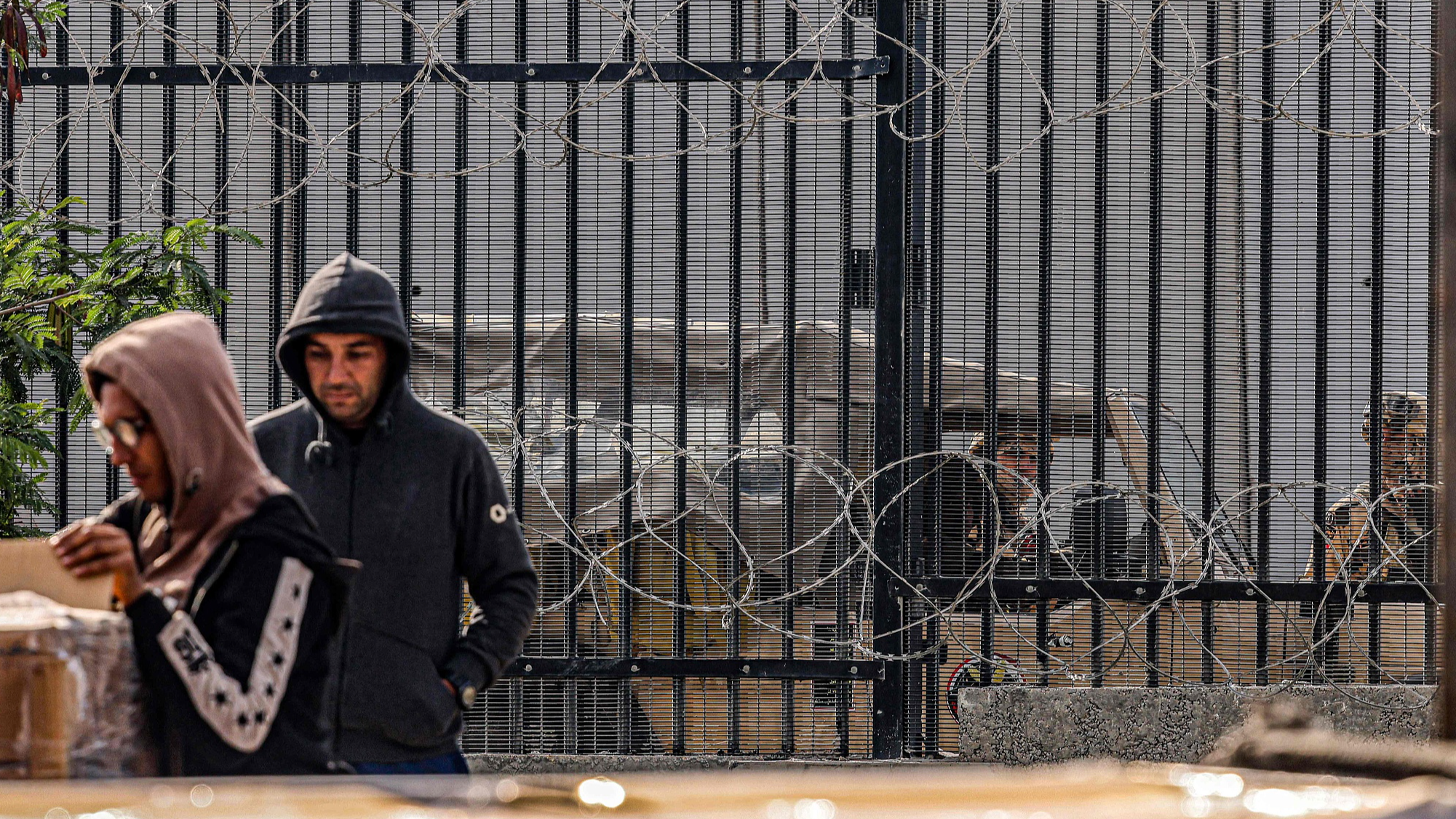 Egyptian army soldiers look on from behind the barbed-wire border fence as Palestinian workers unload crates of humanitarian aid entering the Gaza Strip through the Kerem Shalom border crossing in the southern part of the Palestinian territory on January 29, 2024. /CFP
