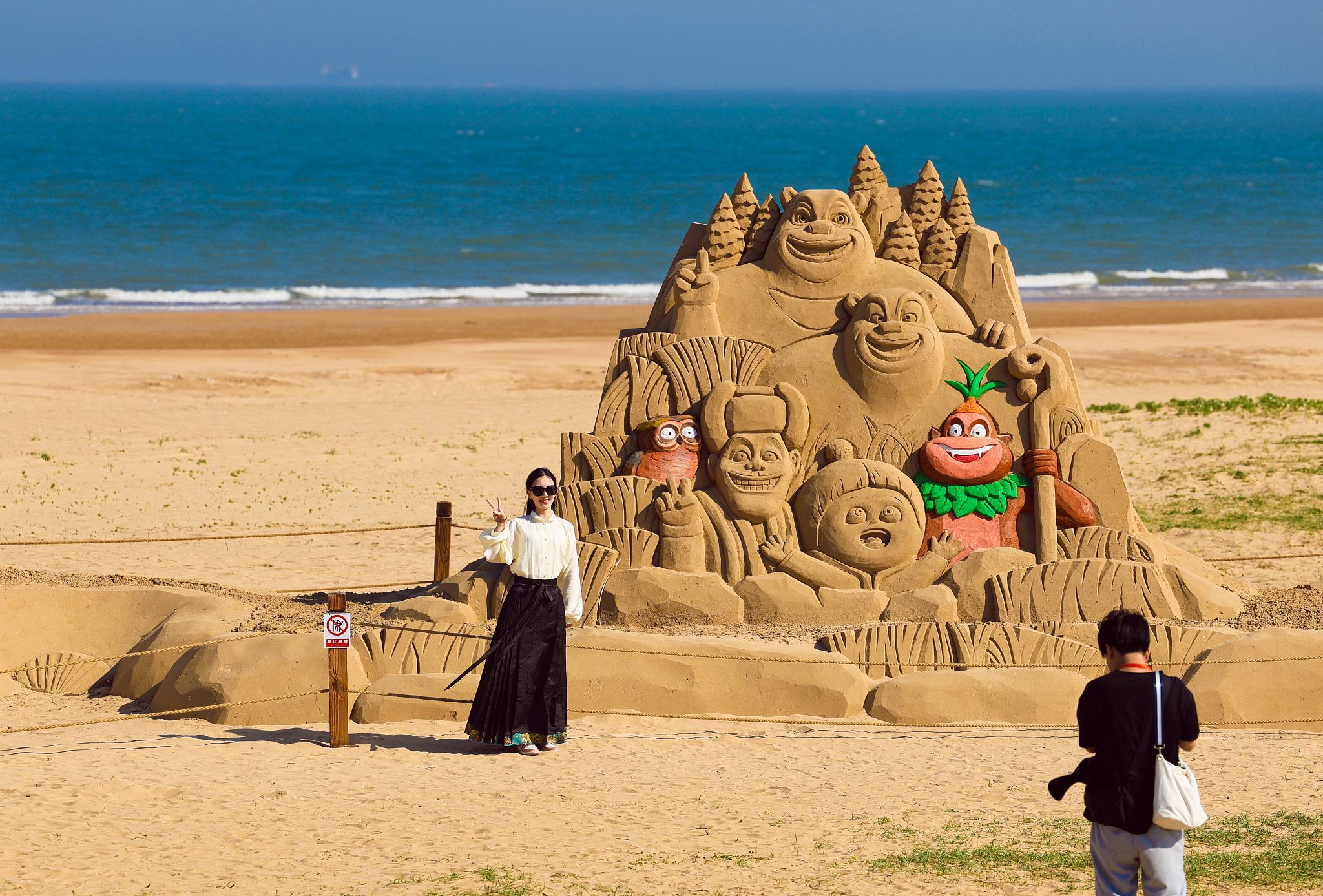 A tourist is seen posing in front of a Bonnie Bears sand sculpture at the Rizhao Seashore National Forest Park in Shandong Province, China, on May 9, 2024. /CFP