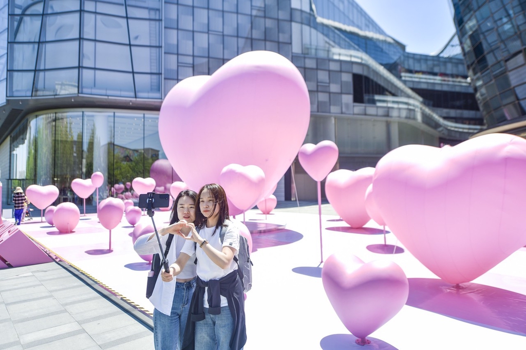 Two women take a selfie with heart-shaped balloons set up in a square outside a mall in Jinan, Shandong Province, May 15, 2024. /IC