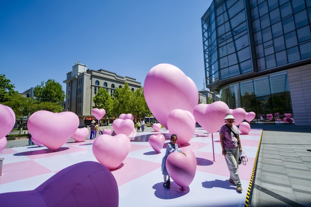 People pass by heart-shaped balloons set up in a square outside a mall in Jinan, Shandong Province, May 15, 2024. /IC