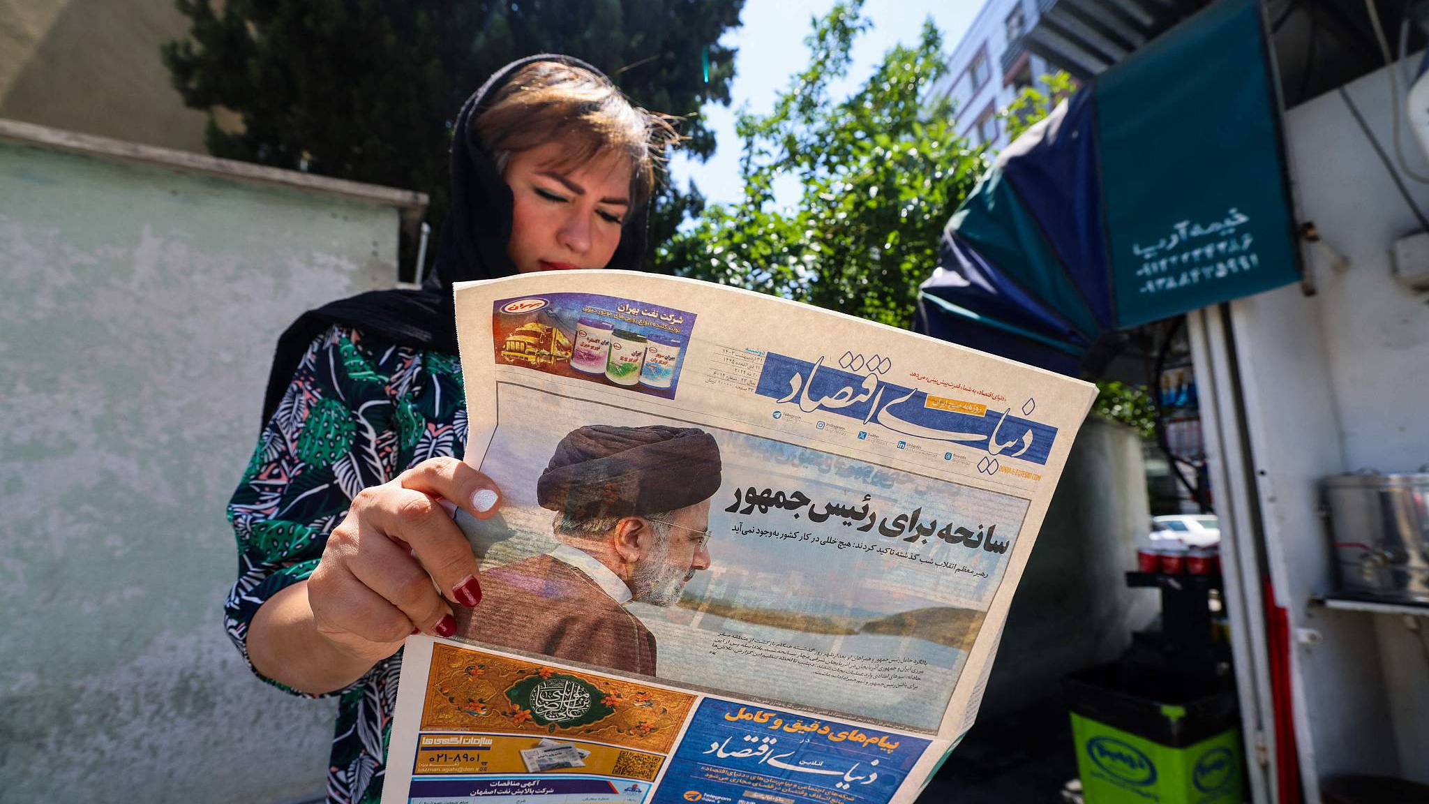A woman reads a newspaper with a front-page report on the crash of the late Iranian President Ebrahim Raisi's helicopter outside a kiosk in Tehran, Iran, May 20, 2024. /CFP 