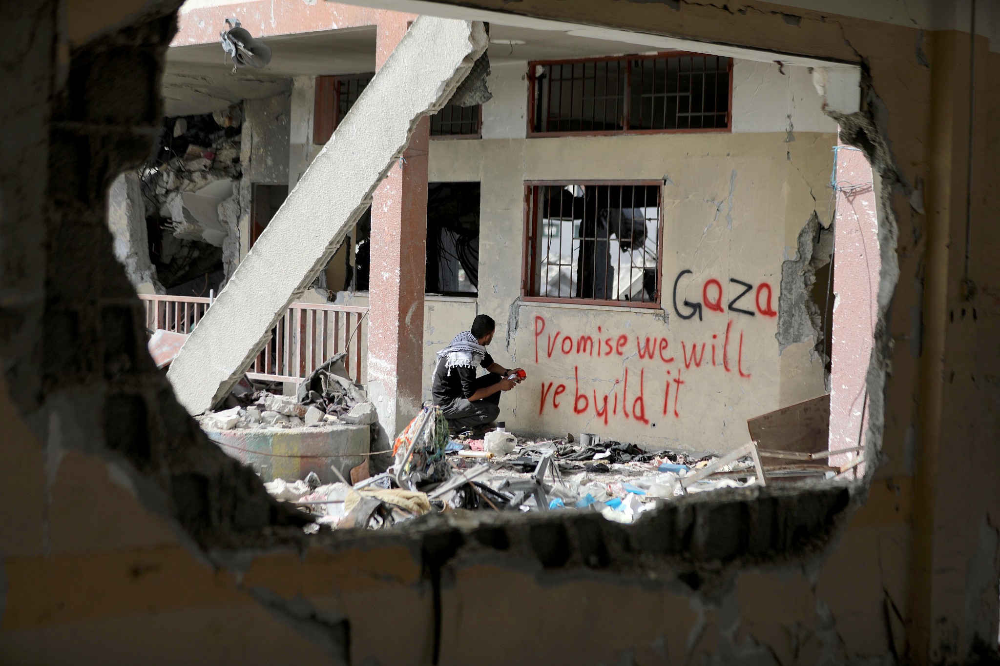 A Palestinian youth writes 'Gaza, promise we will rebuild it' on a building destroyed by the Israeli army in Shuja'iyya neighborhood, Gaza, May 21, 2024. /CFP