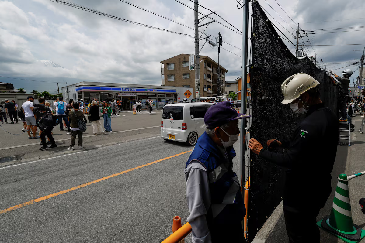 Tourists stand nearby as workers erect a barrier to block the view of a popular Mount Fuji photo spot, near a convenience store in Fujikawaguchiko town, Yamanashi prefecture, Japan, May 21, 2024. /Reuters