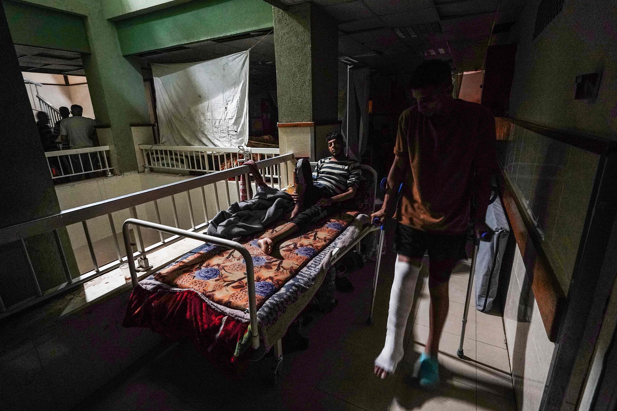 A patient lies in a bed as another walks by in a corridor after a partial power cut at the Al-Aqsa Martyrs Hospital in Deir al-Balah, May 23, 2024. /CFP