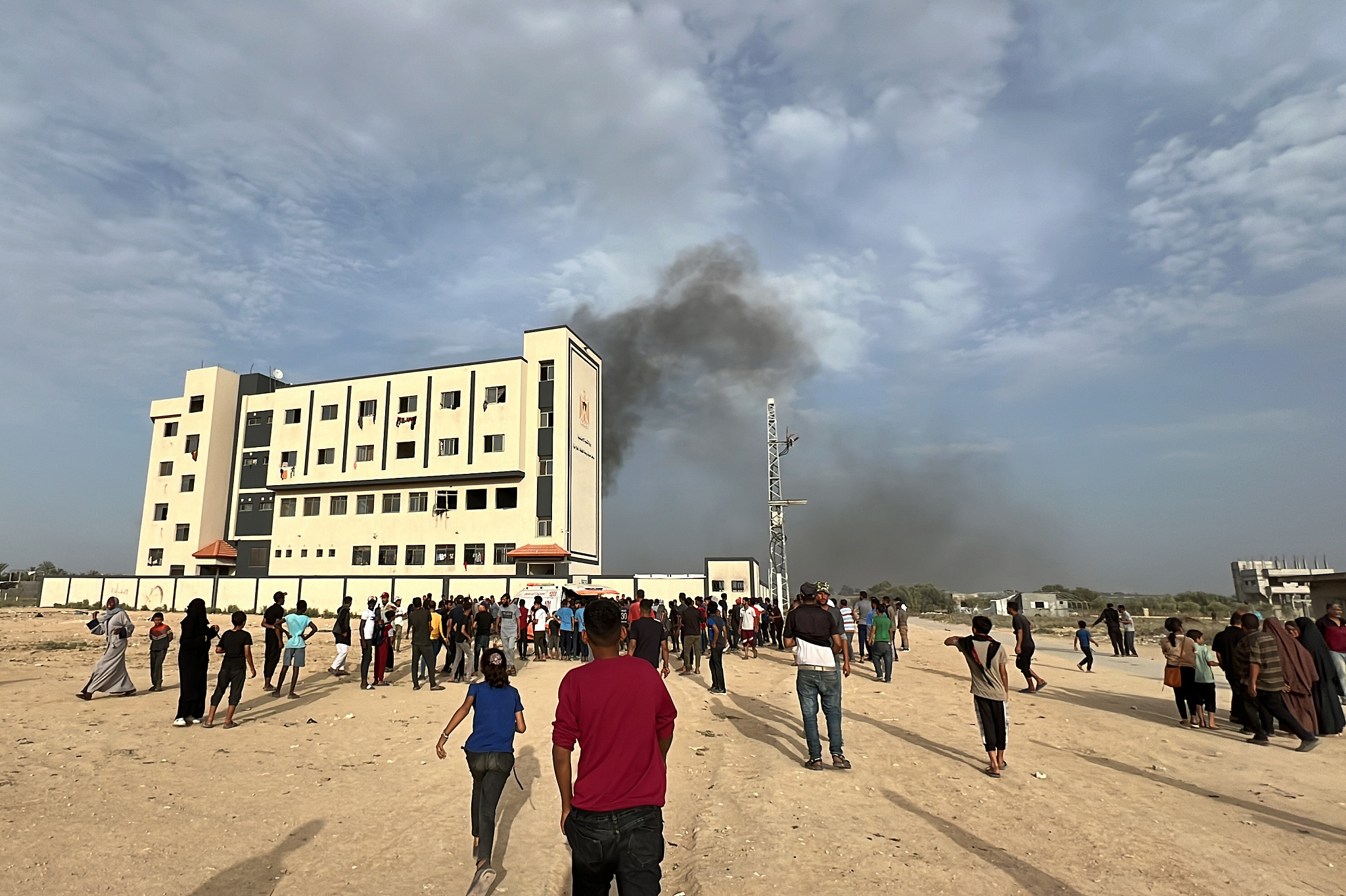 Palestinians gather near a damaged site as smoke rises from a building belonging to the Ministry of Social and Development, where displaced Palestinians are staying, due to the Israeli attacks in Deir Al-Balah, Gaza, May 23, 2024. /CFP