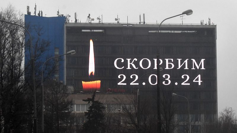 An advertising screen on the facade of a building displays an image of a lit candle and the slogan 