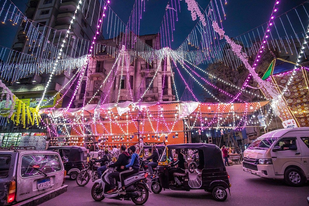 Vehicles, motorcycles, and tuk-tuks (motorised rickshaws) drive past a stall selling Ramadan lanterns along a main street in the northern suburb of Shubra in Egypt's capital Cairo on April 12, 2021, at the start of the Muslim holy fasting month of Ramadan. /CFP