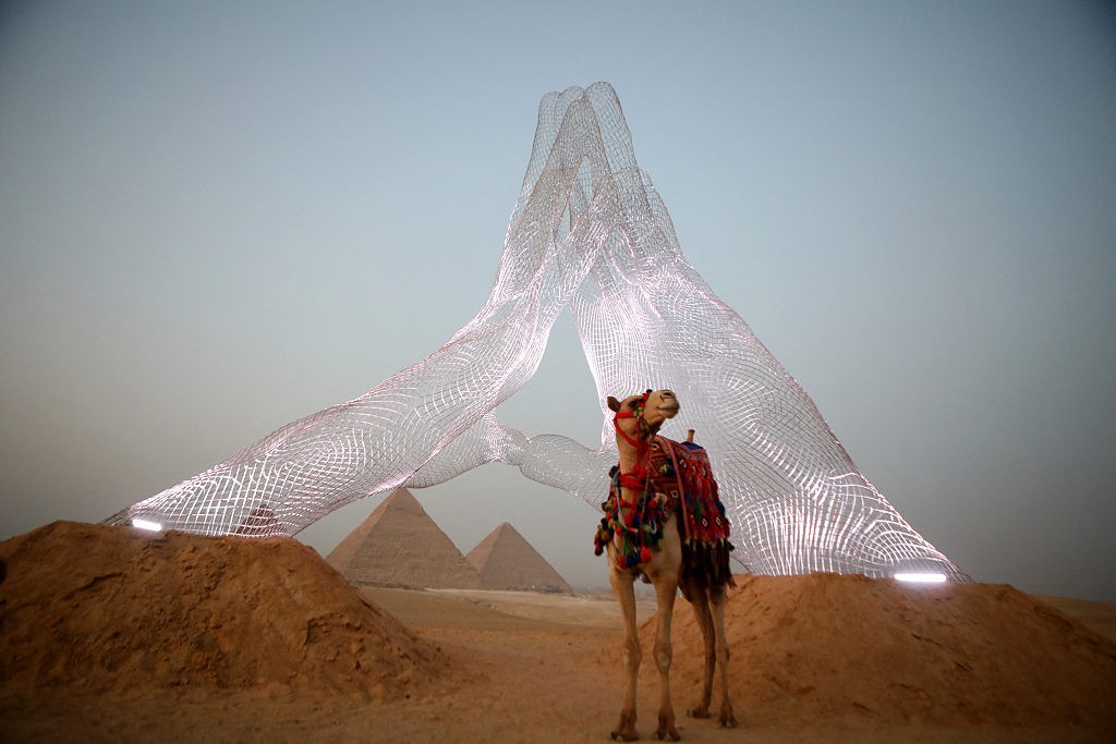 A camel stands next to an installation by Italian artist Lorenzo Quinn entitled Together, facing the pyramids on the Giza Plateau on October 23, 2021. /CFP