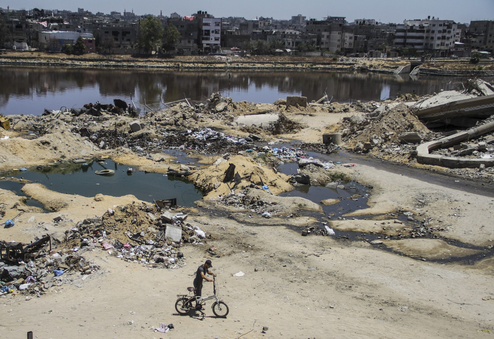 A Palestinian rides bike near Sheikh Radwan Pond as wastewaters and sewage mix into the Pond, Gaza's only source of clean water from rainwater, due to Israeli attacks in Sheikh Radwan district of Gaza City, June 6, 2024. /CFP
