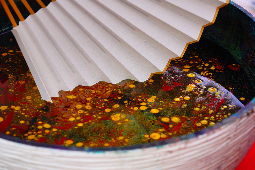 A photo taken on June 8, 2024 in Beijing's Panjiayuan antique market shows the marbling process of a fan using vibrant colors. /CFP