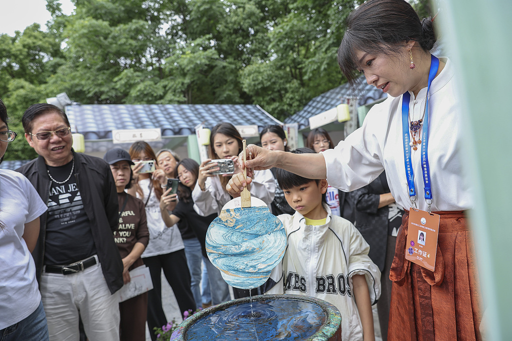 A young visitor to Nantang Pedestrian Street tries out the marbling process with the help of a vendor in Wenzhou, Zhejiang Province, June 6, 2024. /CFP