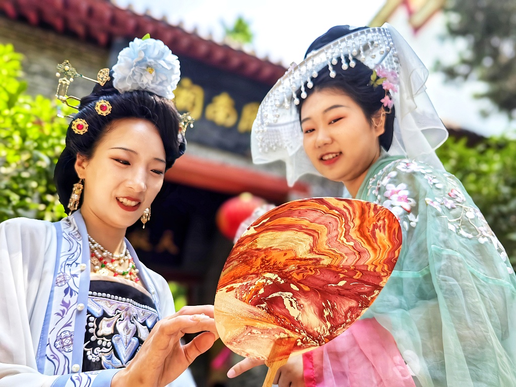 Two young women wearing traditional Chinese attire appreciate a marble fan in Luoyang, June 11, 2024. /CFP