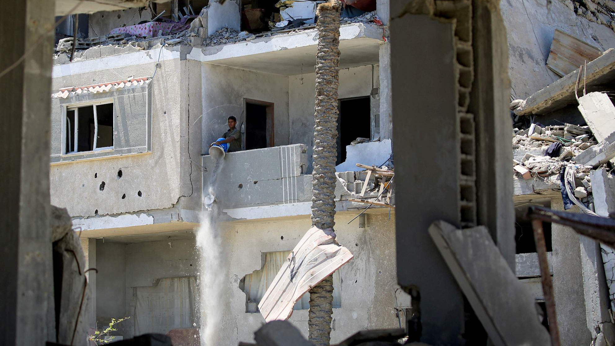 A Palestinian man empties a bucket of debris from an apartment in a building destroyed by Israeli bombardment in Khan Yunis, southern Gaza Strip, June 11, 2024. /CFP