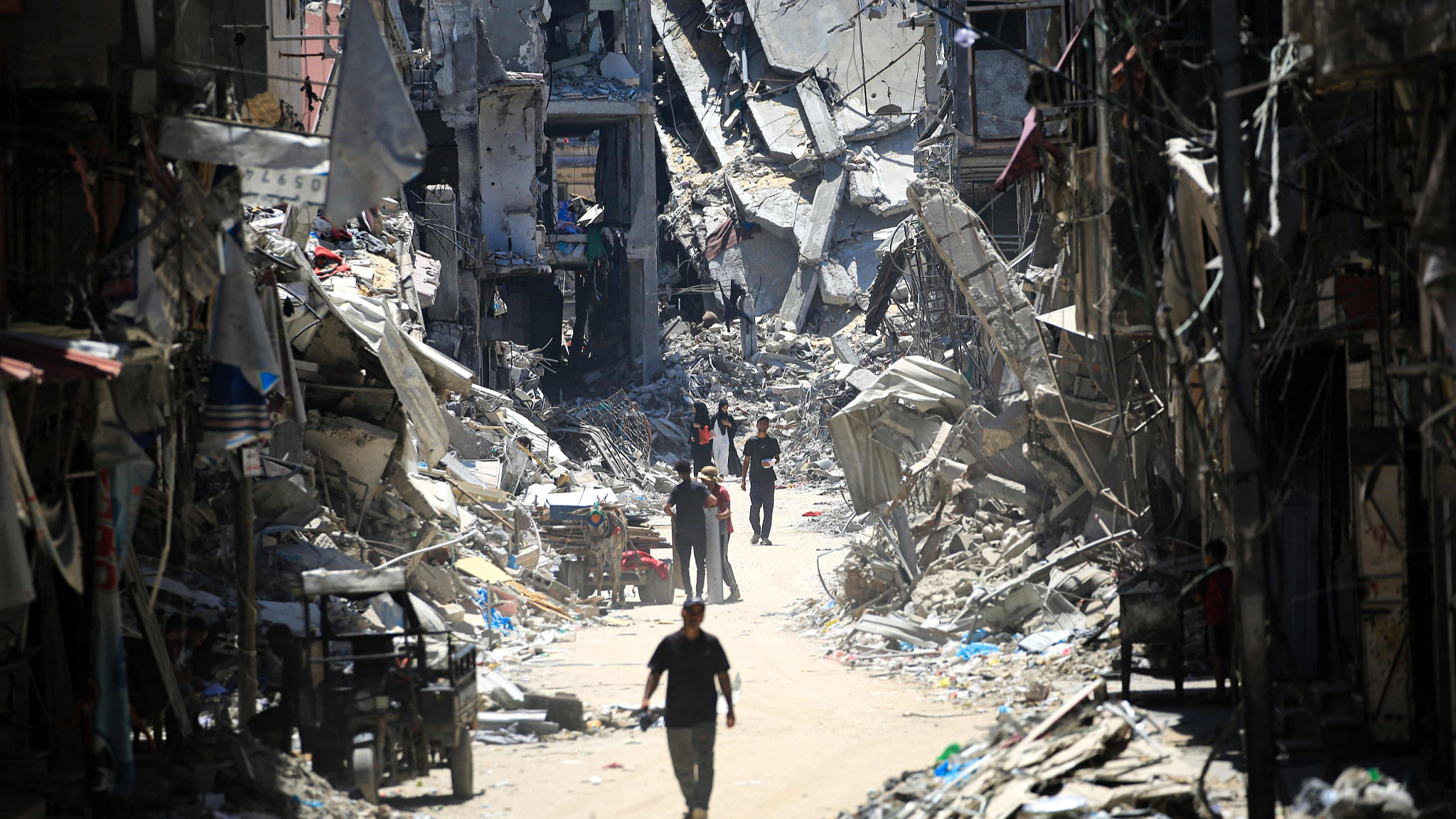 Palestinian men walk along a narrow street past destroyed buildings in Khan Yunis, in the southern Gaza Strip on June 11, 2024, amid the ongoing conflict between Israel and the Palestinian Hamas group. /CFP