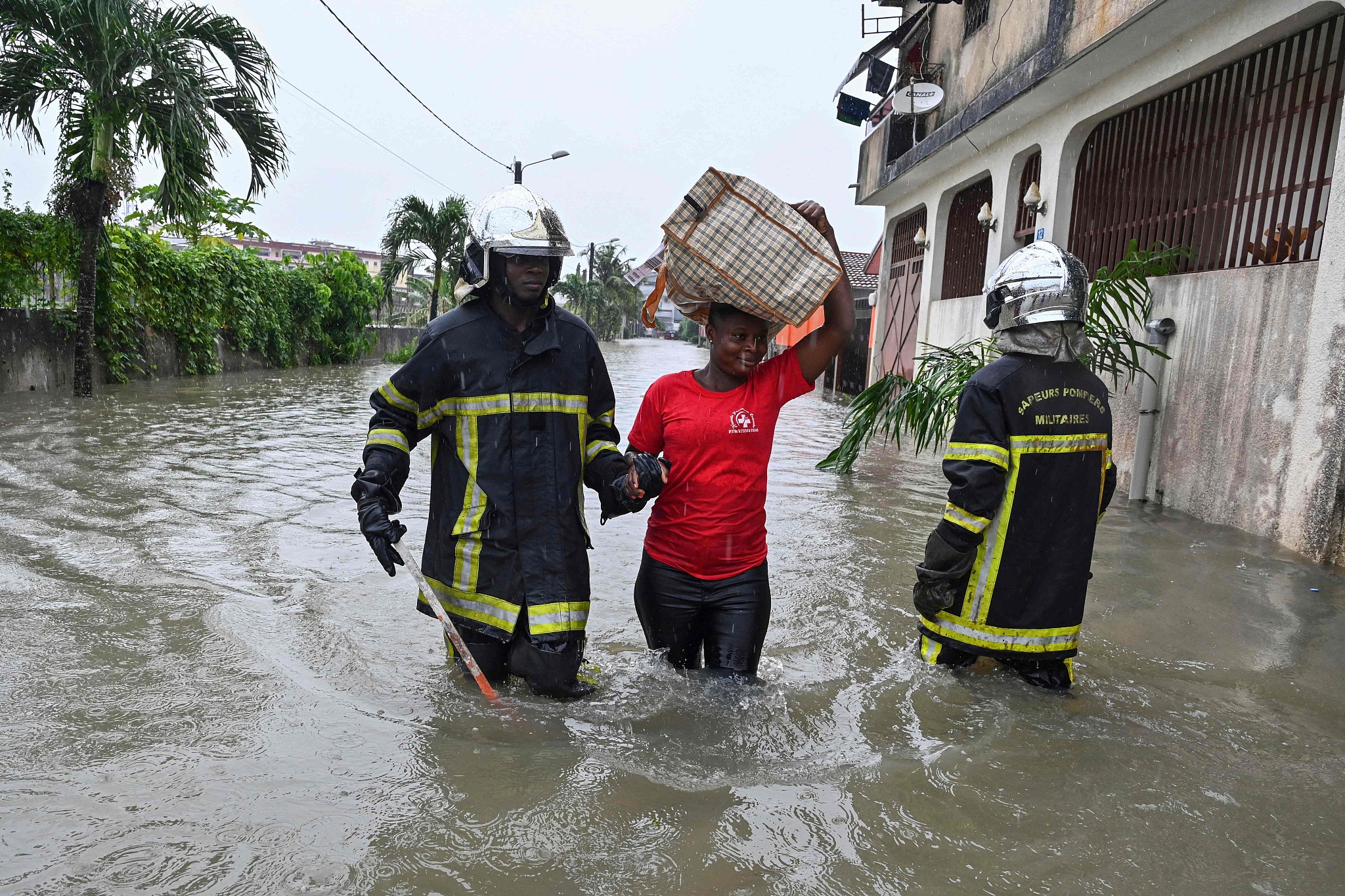 A firefighter guides a resident through flood water after torrential rains in Cocody Angre, Abidjan, June 14, 2024. /CFP