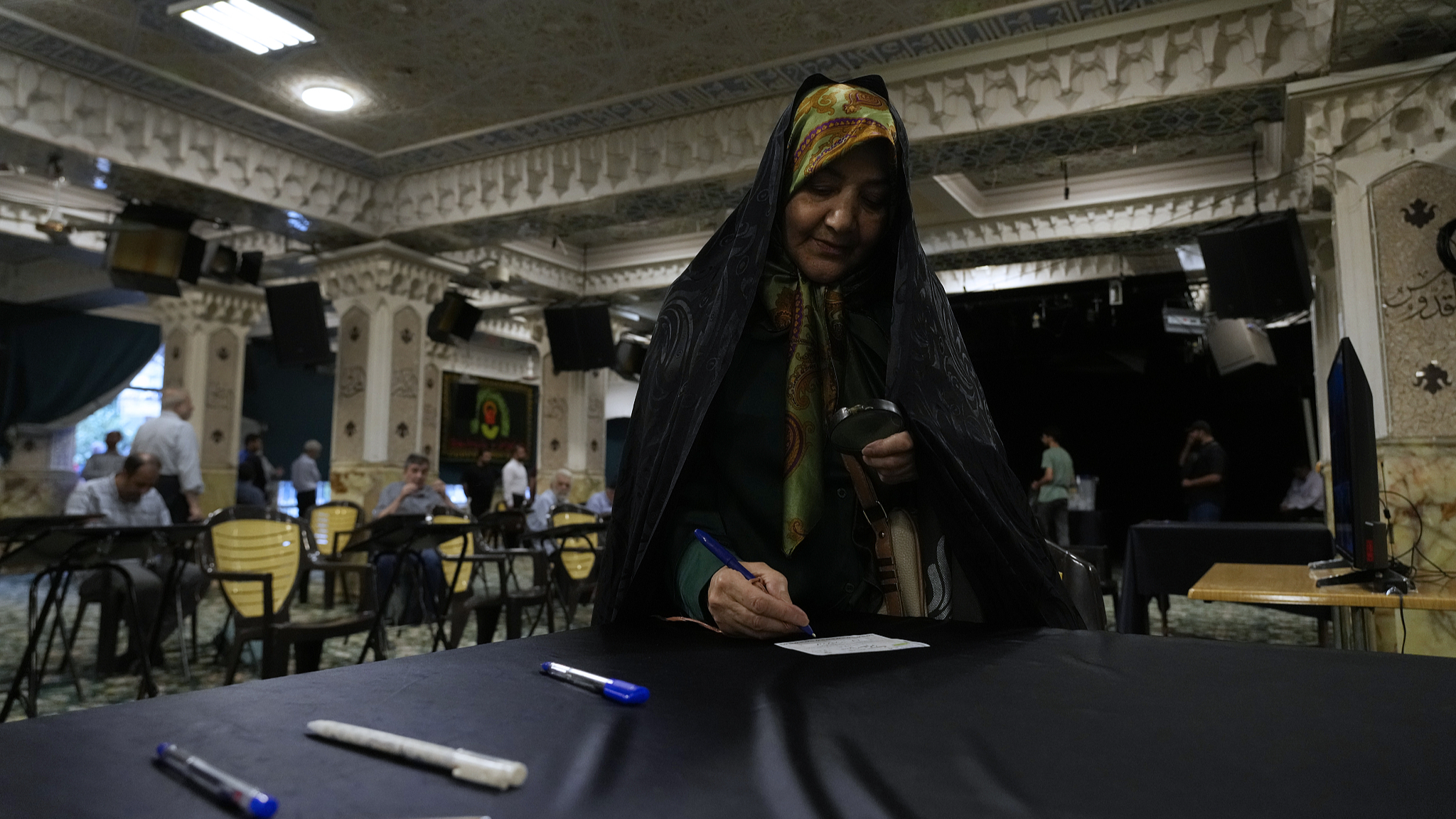 An elderly woman uses a magnifying glass to fill out her ballot for the presidential election at a polling station in Tehran, Iran, June 28, 2024. /CFP