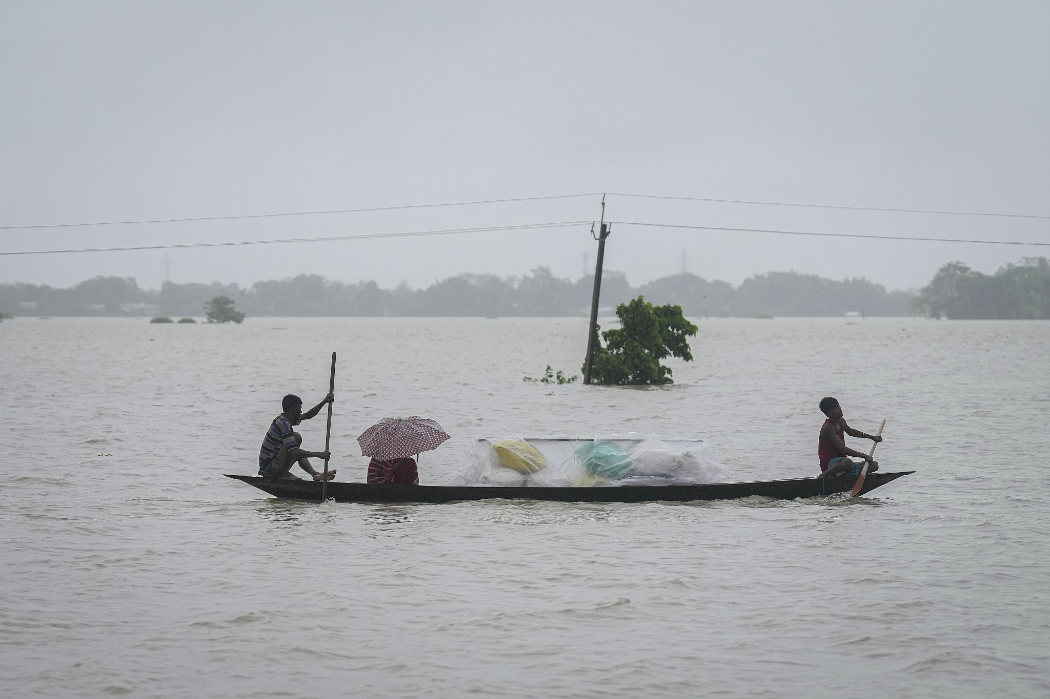 Flood-affected people travel through floodwaters with their belongings in Sildubi village, Morigaon district in the northeastern state of Assam, India, July 2, 2024. /CFP