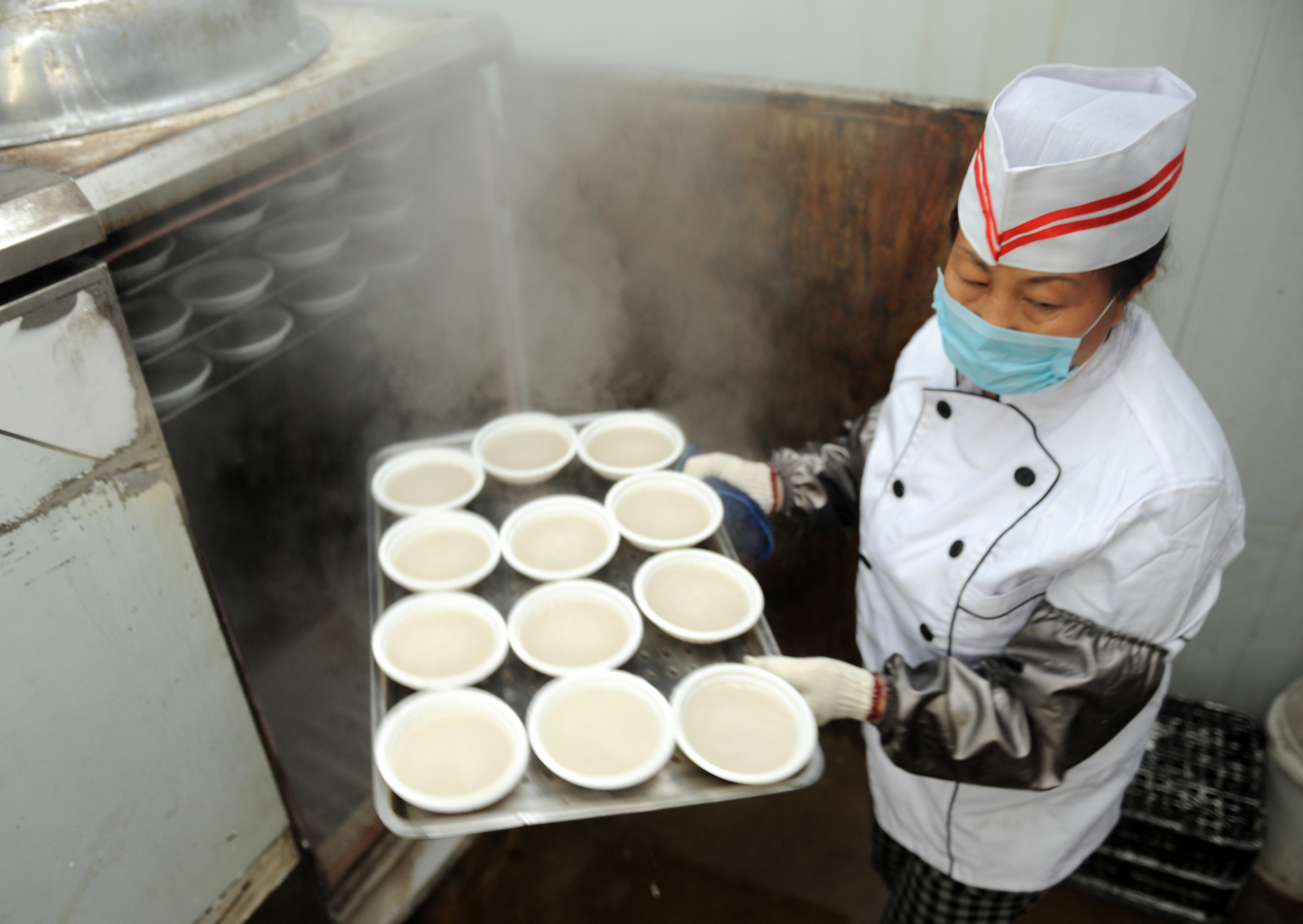 A cook takes a tray of wantuan out of a steaming oven. /IC