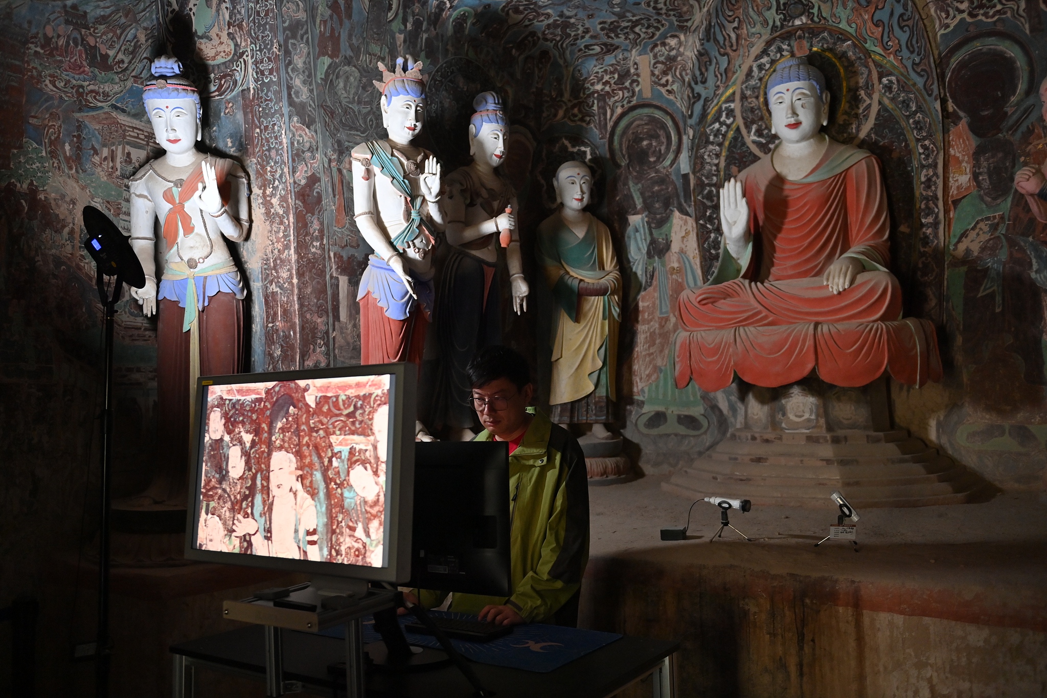 A photo captures a staff from the Dunhuang Research Academy conducting on-site inspection of digital images of Dunhuang murals inside one of the Mogao Grottoes, in Jiuquan, Gansu Province, on June 5, 2024. /CFP