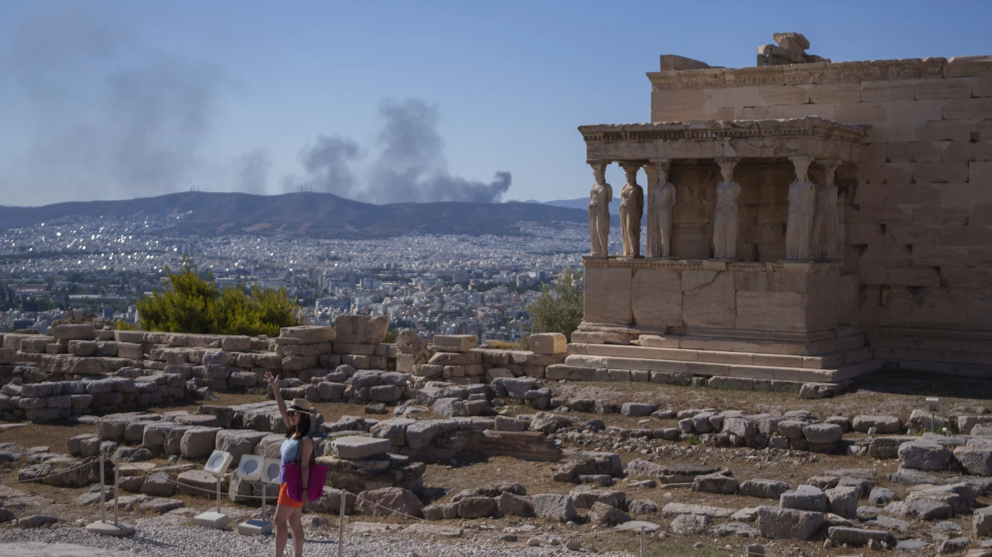 A woman poses in front of Caryatid statues amid a heat wave. Smoke can be seen from a fire, during a hot, windy day at Acropolis Hill in Athens, July 16, 2024. /AP