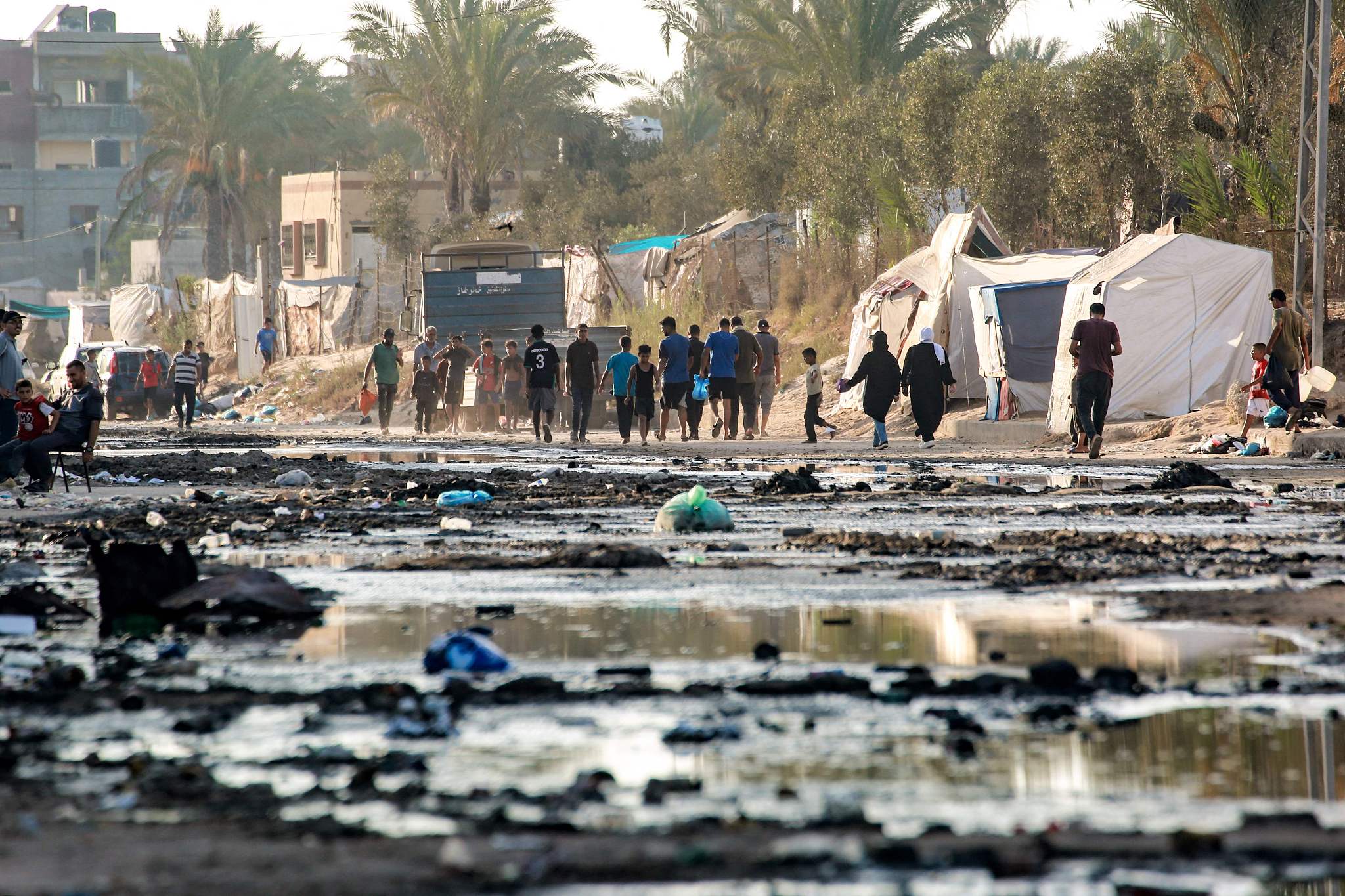 Palestinians walk near tents used as shelter along a street covered with stagnant wastewater in Deir el-Balah in the central Gaza Strip, July 19, 2024. /CFP