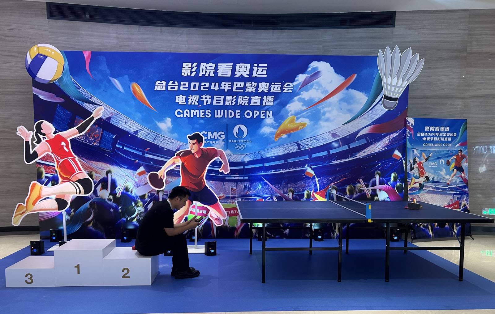 A man sits in front of a poster announcing the introduction of live broadcasts from Paris Olympics in cinemas across China on Monday, July 22, 2024. /CGTN