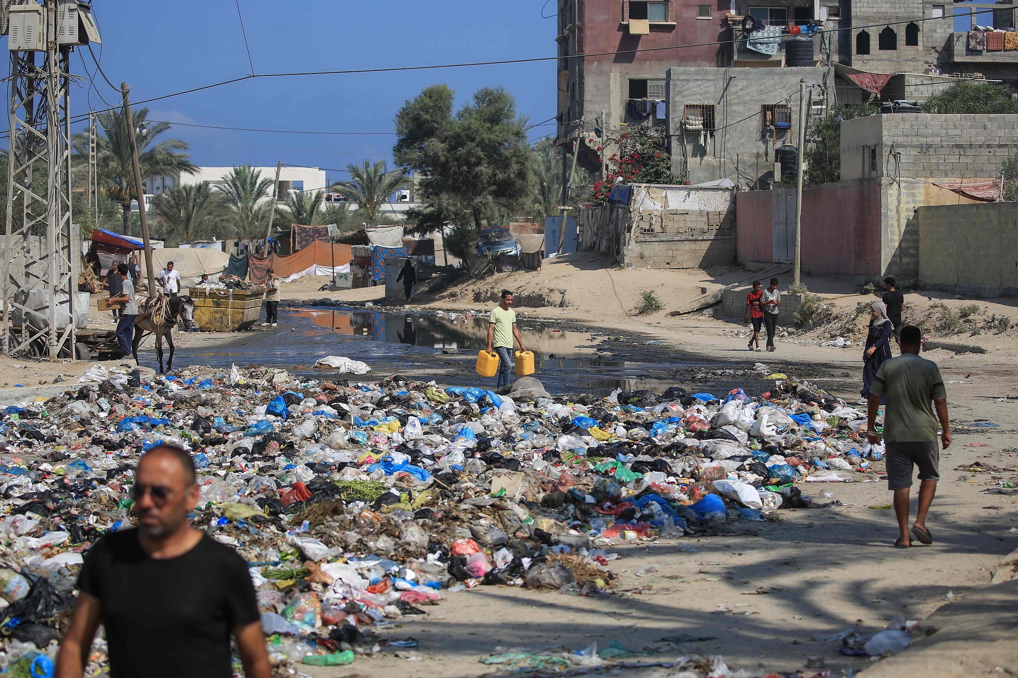 Palestinians walk past sewage water and a garbage dump on a street in Deir el-Balah in the central Gaza Strip, as municipal infrastructures fail due to Israeli bombardment of the besieged Palestinian territory, July 23, 2024. /CFP
