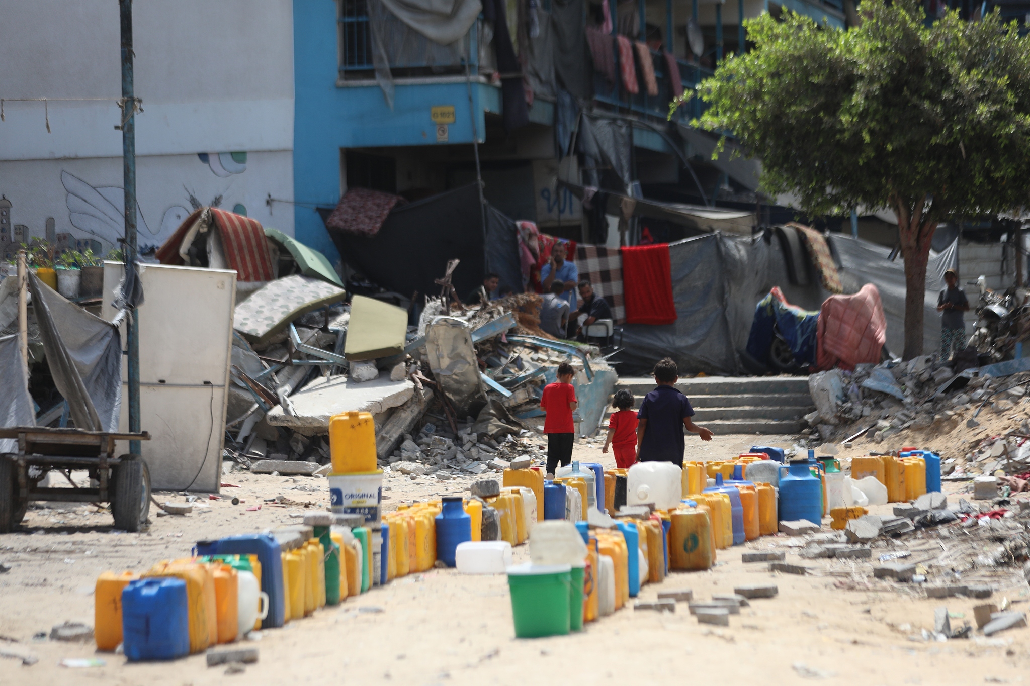 Palestinian kids are seen near water drums as epidemics spread rapidly due to large crowds in displaced civilians' shelters, the lack of garbage collection on the roads, insufficient drinking water and water for daily use, and the inability to meet the need for personal hygiene in the Gaza Strip, July 26, 2024. /CFP