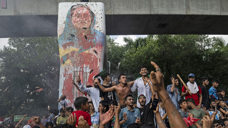 Protesters celebrate beside a defaced portrait of Prime Minister Sheikh Hasina after news of her resignation, in Dhaka, Bangladesh, August 5, 2024. /CFP