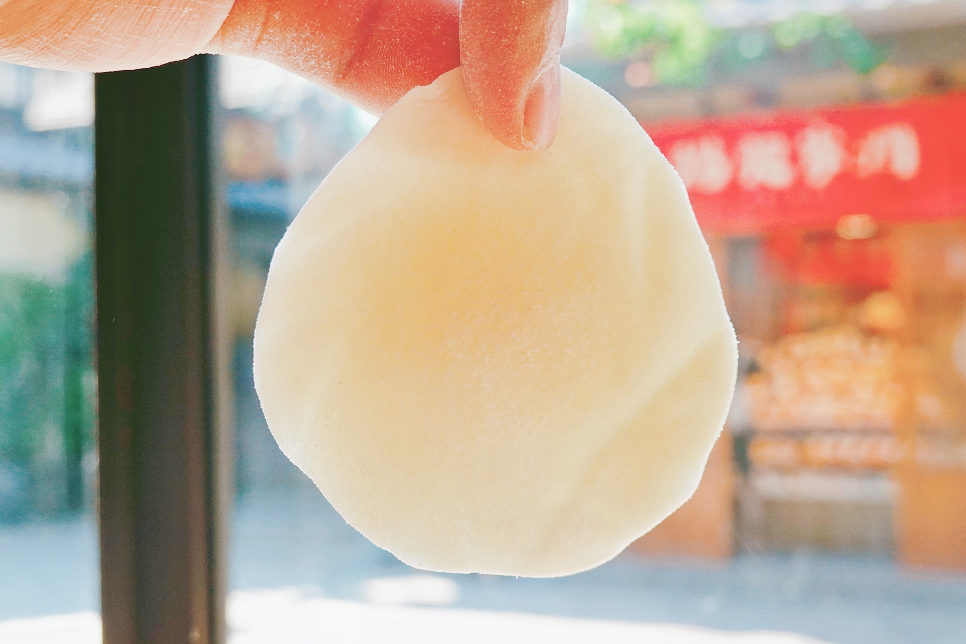 A Wuxi-style steamed bun wrapper is held up, featuring a thick center and thinner edges. /CGTN