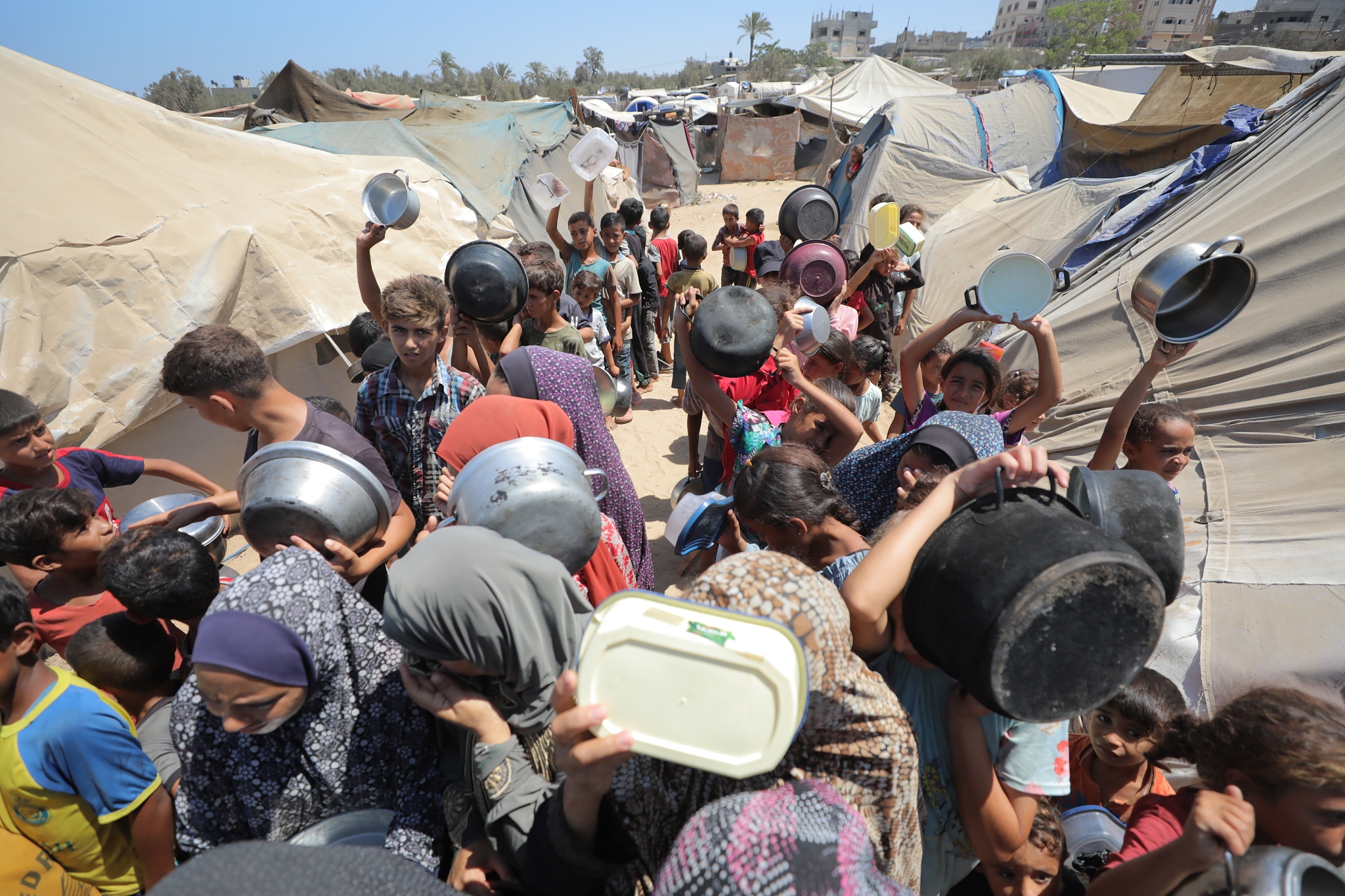 Palestinians wait in line to receive food distributed by charities while Israeli attacks on the Gaza Strip continue unabated in Deir al-Balah, August 7, 2024. Due to the complete embargo imposed on the area, Palestinians are unable to secure many essential needs, including basic food supplies. /CFP
