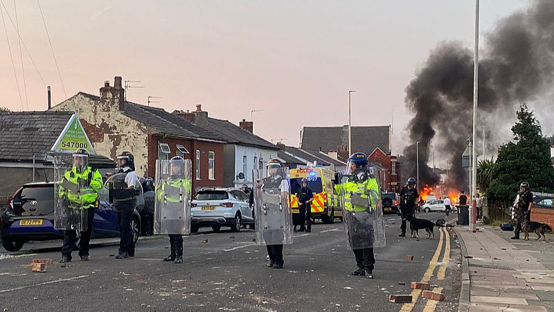 Asap mengepul dari kebakaran yang dimulai oleh pengunjuk rasa saat polisi antihuru-hara berjaga setelah kerusuhan di dekat Masjid Southport Islamic Society di Southport, Inggris barat laut, 30 Juli 2024. /CFP