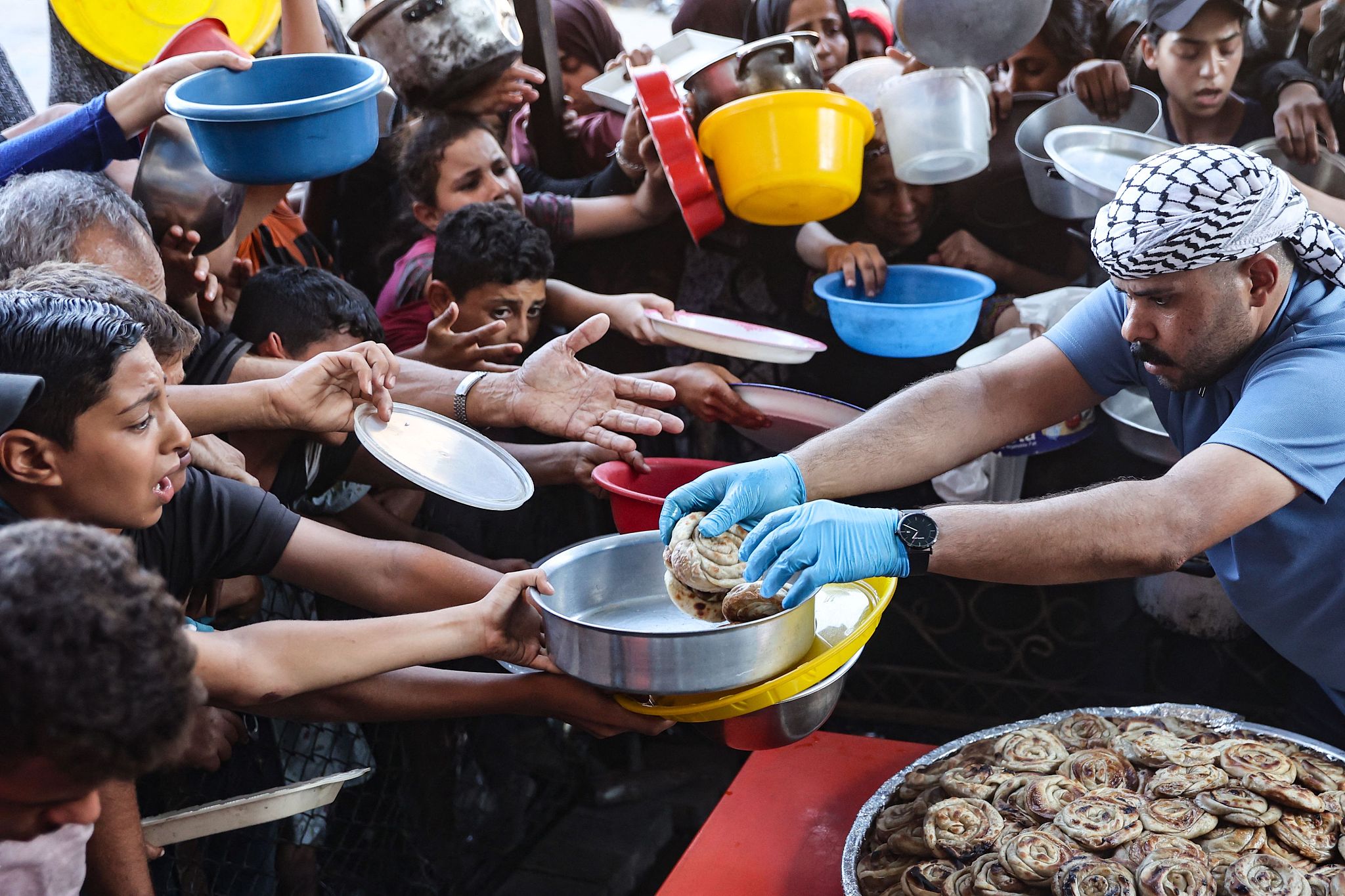 Palestinian children hold out plates to receive their share of vegetable patties prepared by volunteers in Beit Lahia in the northern Gaza Strip, August 14, 2024. /CFP