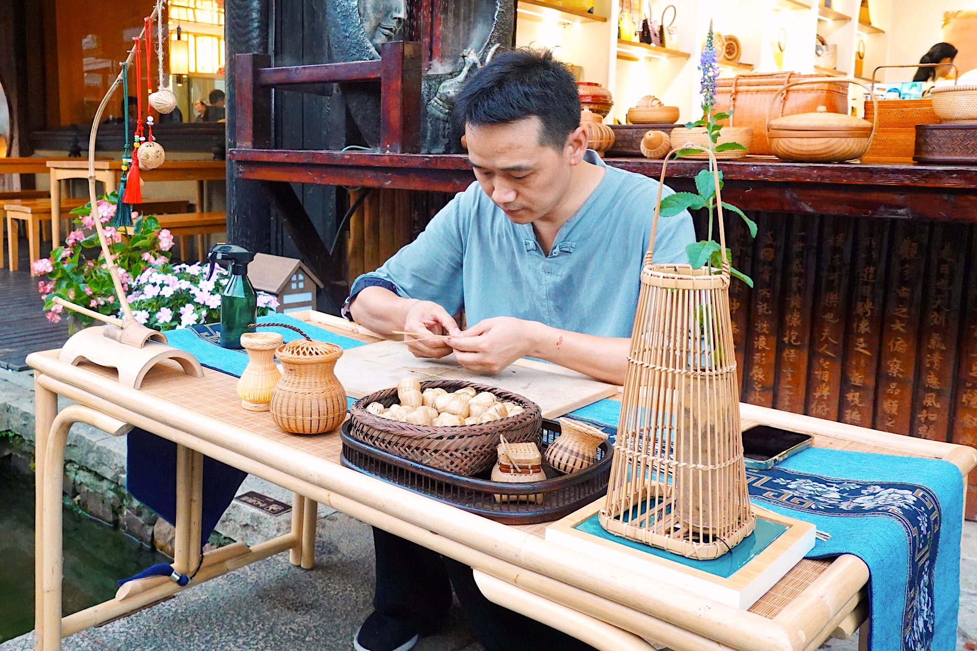 Bamboo craftsman Shi Huihua demonstrates his skills in front of a store in Nianhuawan, a popular tourist town in Wuxi, Jiangsu Province, on July 21, 2024. /CGTN