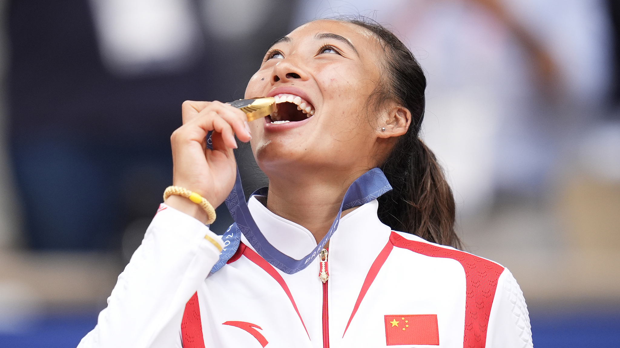 China's Zheng Qinwen bites her gold medal after winning the women's singles tennis final at the Roland Garros at the Olympics in Paris, France, August 3, 2024. /CFP