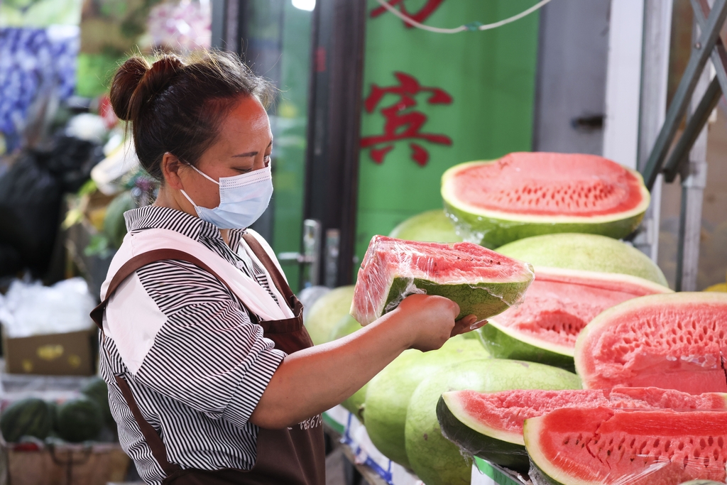 A woman wraps a piece of watermelon at a stall in a fruit market in Manzhouli, Inner Mongolia on August 15, 2024. /IC