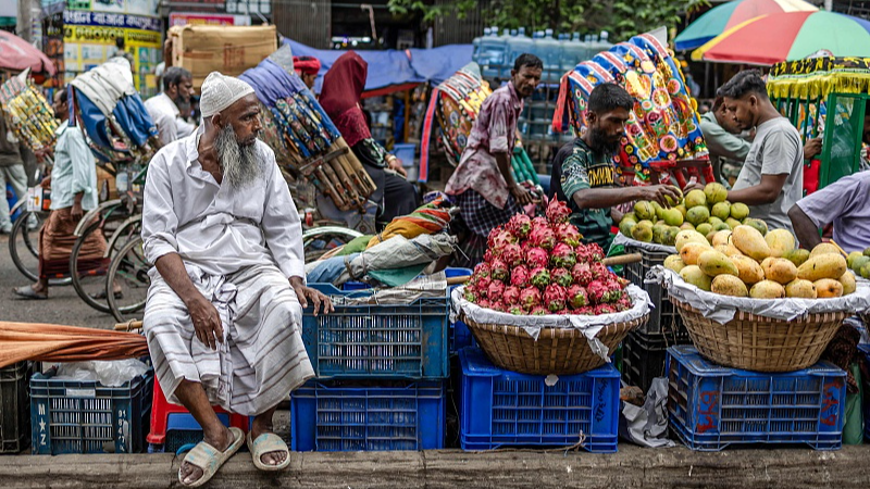 Rickshaw pullers ride past a fruit vendor along a street in Old Dhaka, Bangladesh, August 17, 2024. /CFP