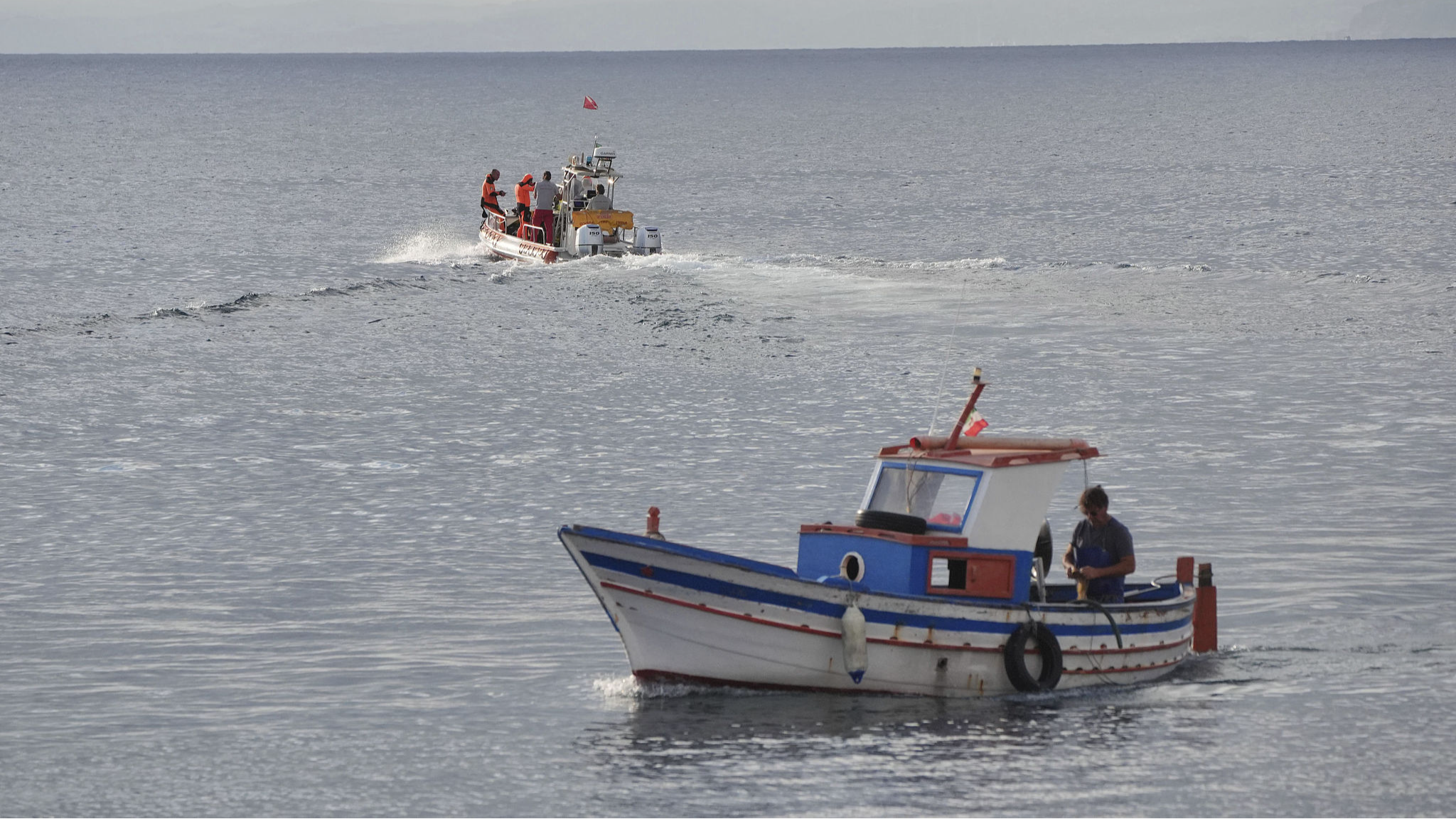 A boat, top, carrying a dive team passes a fishing boat as it heads out to the site of the Bayesian on the fourth day of the search and recovery operation after the luxury yacht sank in a storm on Monday while moored around half a mile off the coast of Porticello, Sicily, August 22, 2024. /CFP