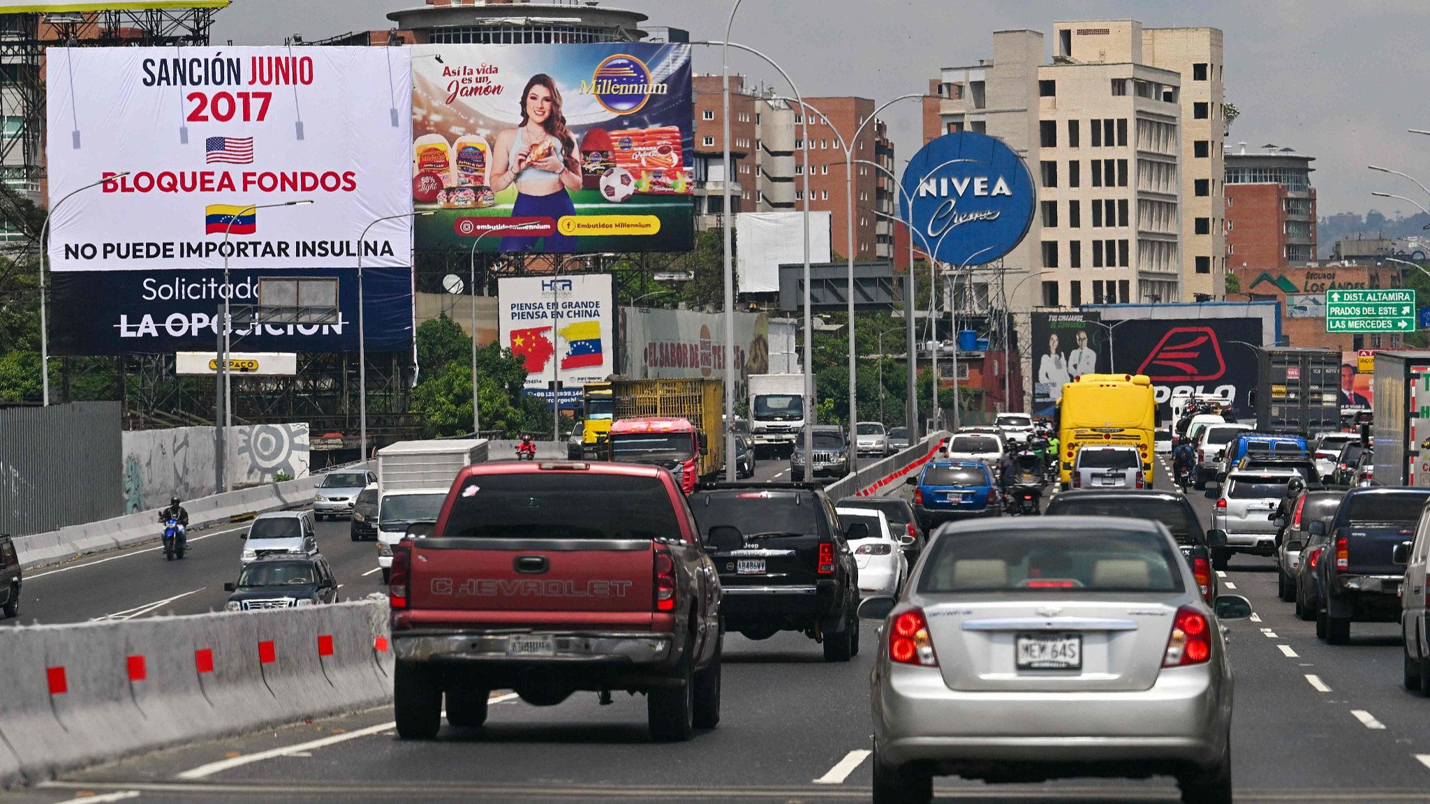 Cars drive past a billboard (L) with a message blaming the opposition for U.S. sanctions to Venezuela, in Caracas on April 16, 2024./ CFP 