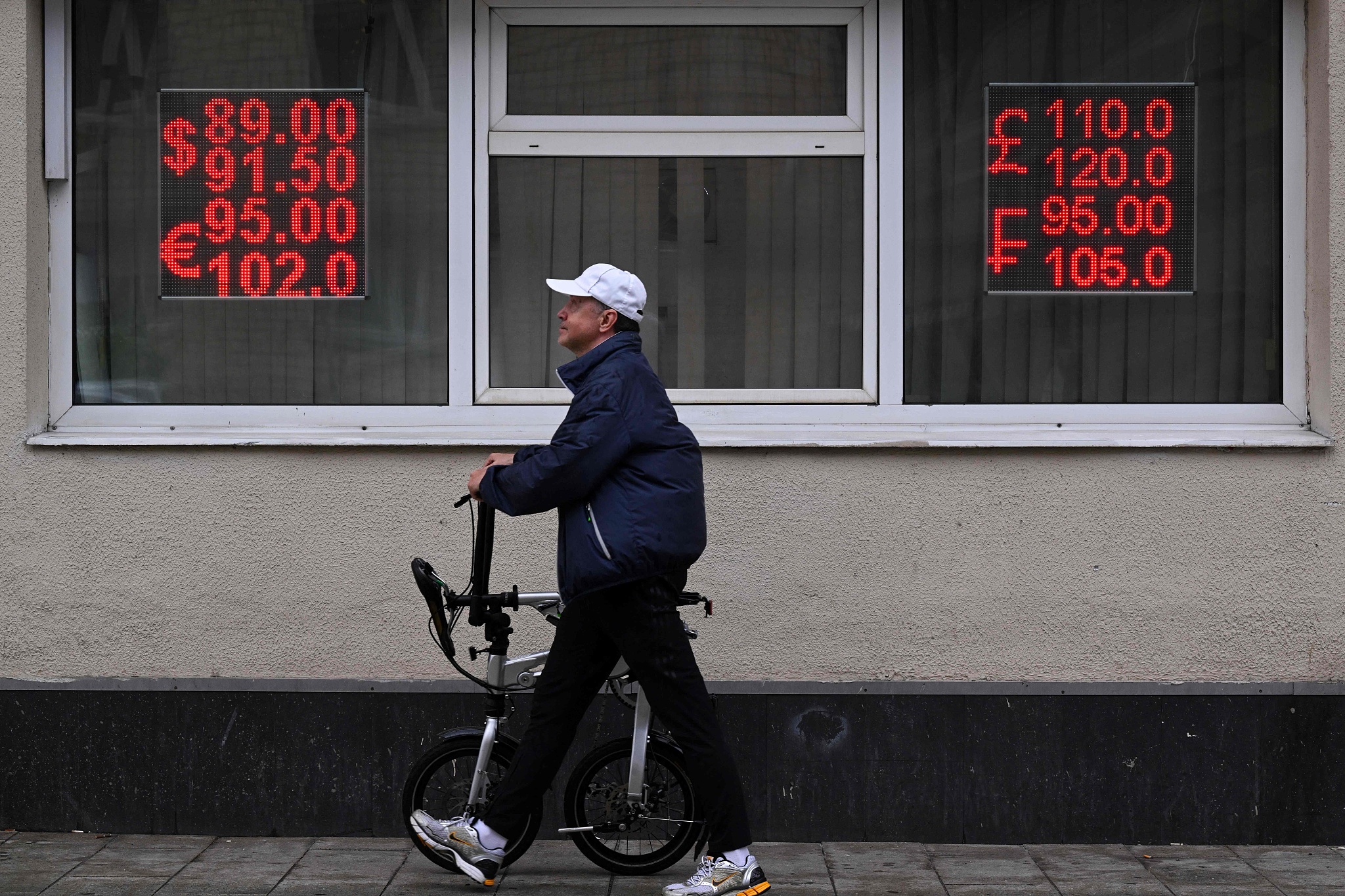 A man walks with a bicycle past a currency exchange office in Moscow on June 13, 2024./ CFP