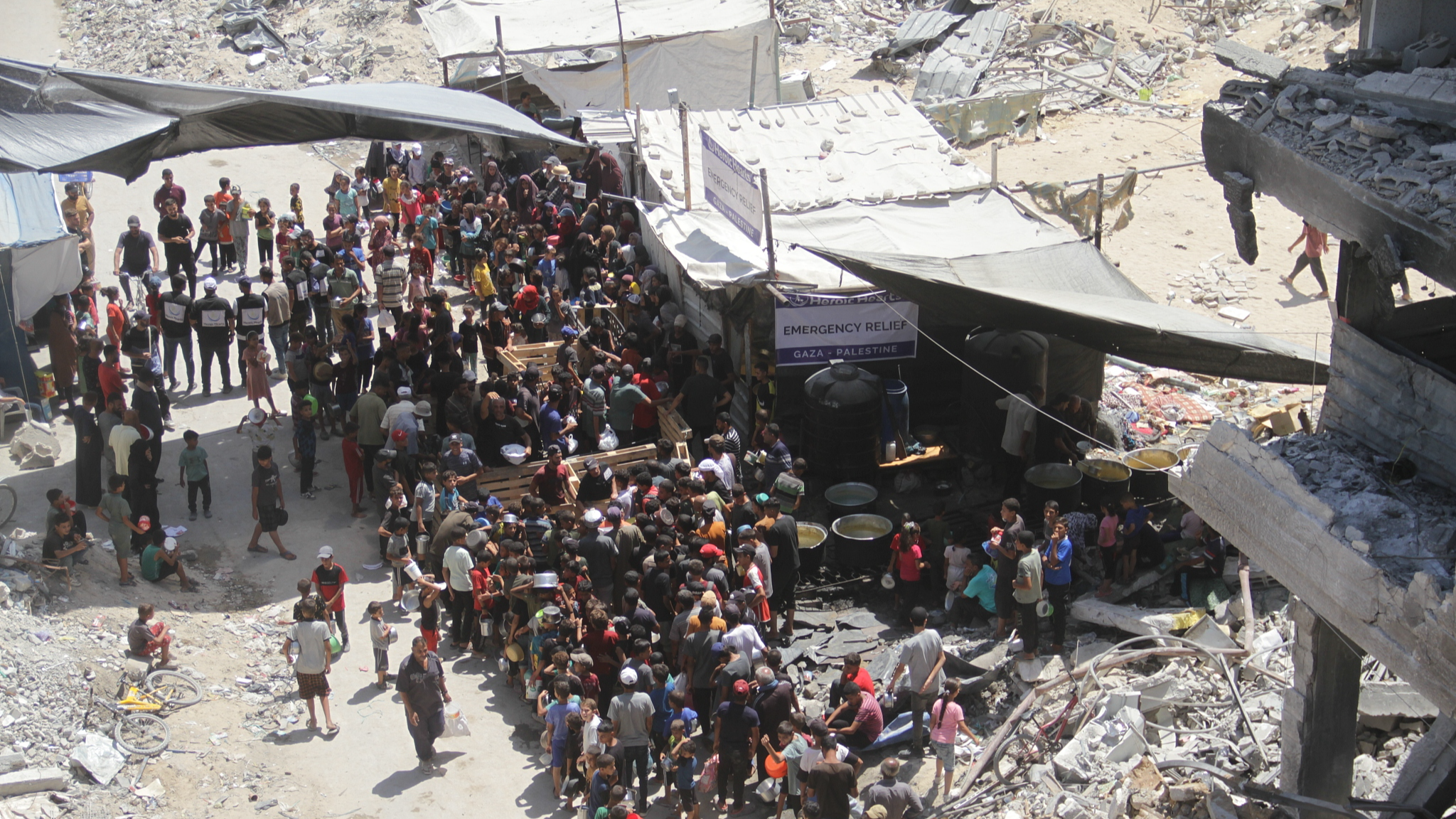 Displaced Palestinians who escaped from Israeli army attacks and took shelter in the Jabalia Refugee Camp in the north of the Gaza Strip line up among the collapsed and heavily damaged buildings to receive food, distributed by charity organizations in Jabalia, Gaza, August 26, 2024. /CFP