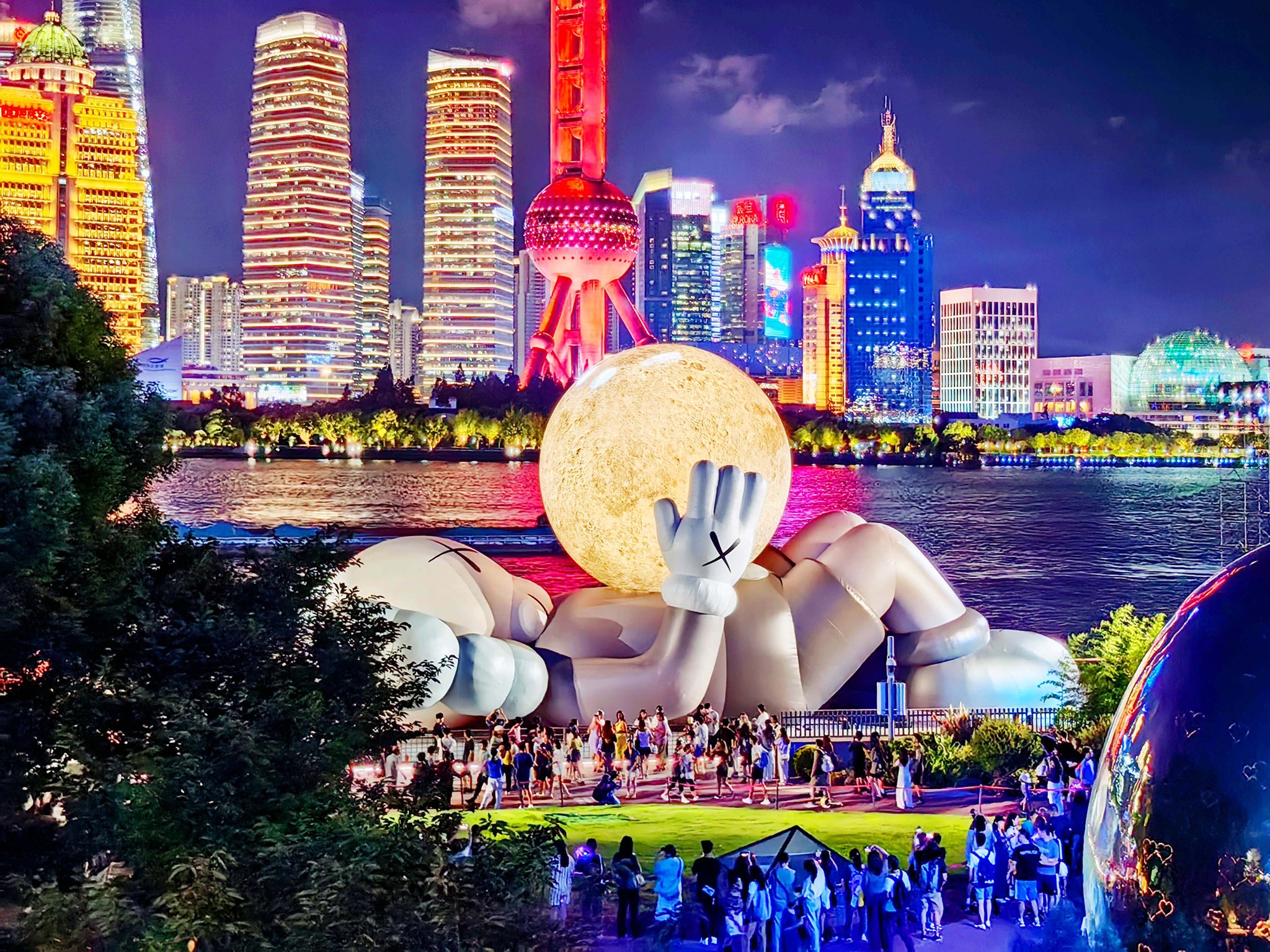 A giant inflatable sculpture by KAWS, featuring this American artist's iconic Companion figure cradling a glowing moon and gazing toward the sky, draws crowds to the North Bund in Shanghai on August 29, 2024. /CFP