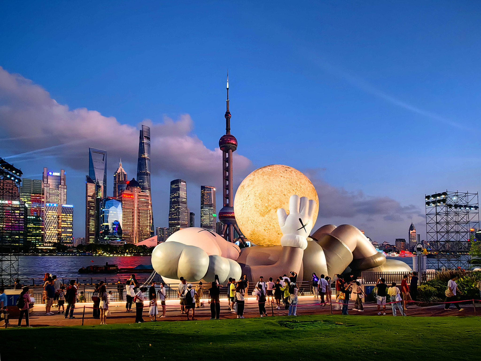 A giant inflatable sculpture by KAWS, featuring this American artist's iconic Companion figure cradling a glowing moon and gazing toward the sky, draws crowds to the North Bund in Shanghai on August 29, 2024. /CFP