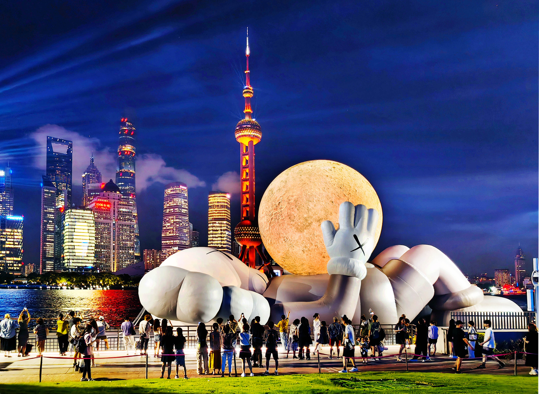 A giant inflatable sculpture by KAWS, featuring this American artist's iconic Companion figure cradling a glowing moon and gazing toward the sky, draws crowds to the North Bund in Shanghai on August 29, 2024. /CFP