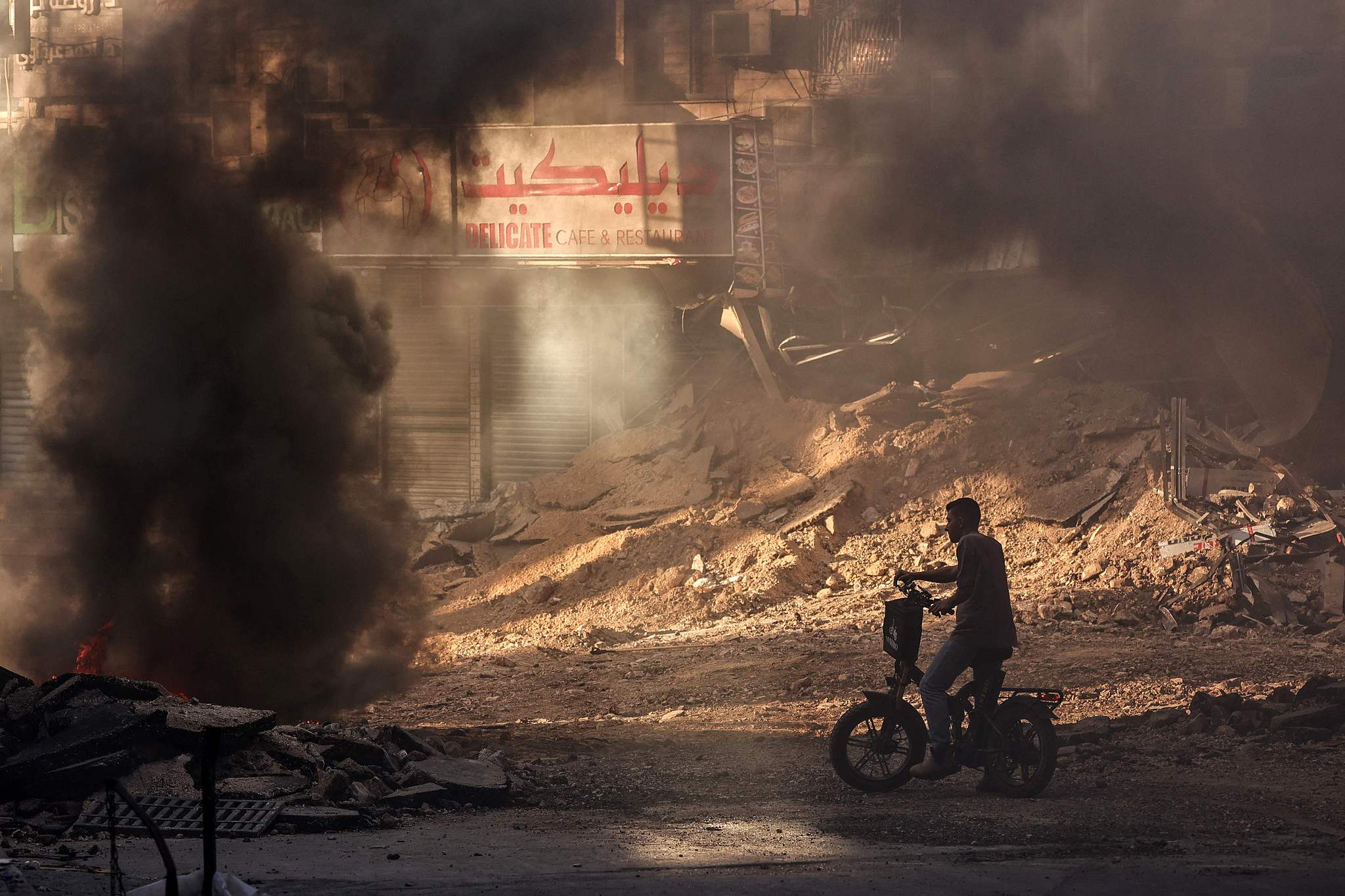 A Palestinian sits on a bike amid an Israeli military raid in a devastated street in Jenin, West Bank, where youths have set tires ablaze, September 4, 2024. /CFP