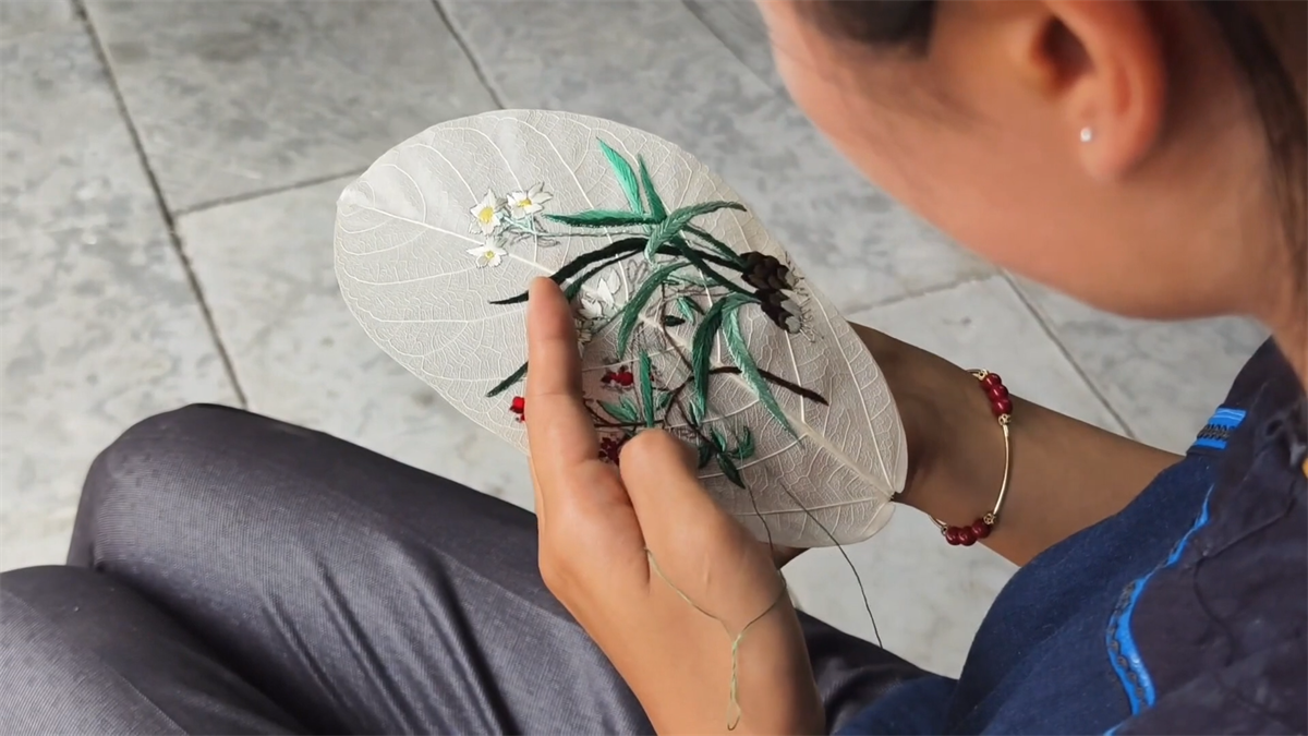 Yang Li's apprentice embroiders orchids on a piece of leaf-vein at a workshop in Tongren City, Guizhou Province. /Photo provided to CGTN